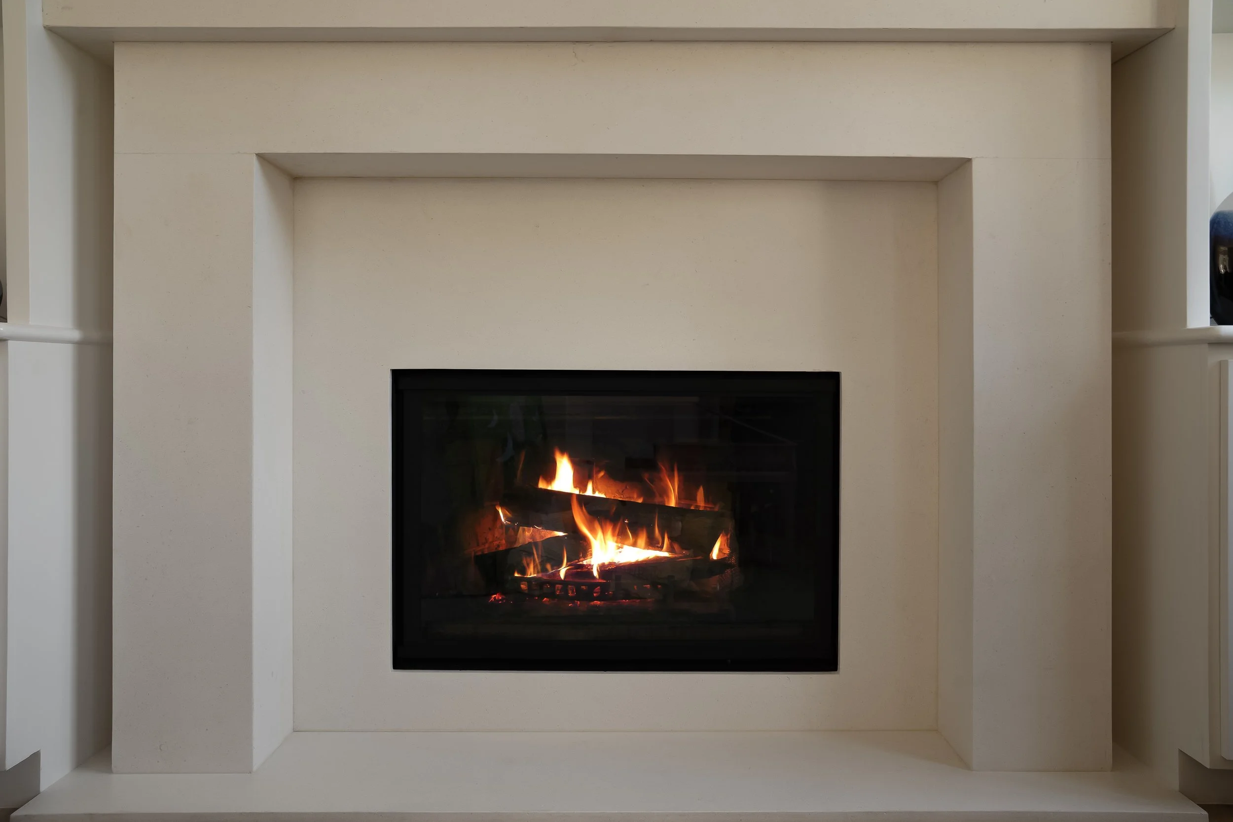 A modern white fireplace with a burning fire inside, mounted on a white wall with built-in shelves on each side.