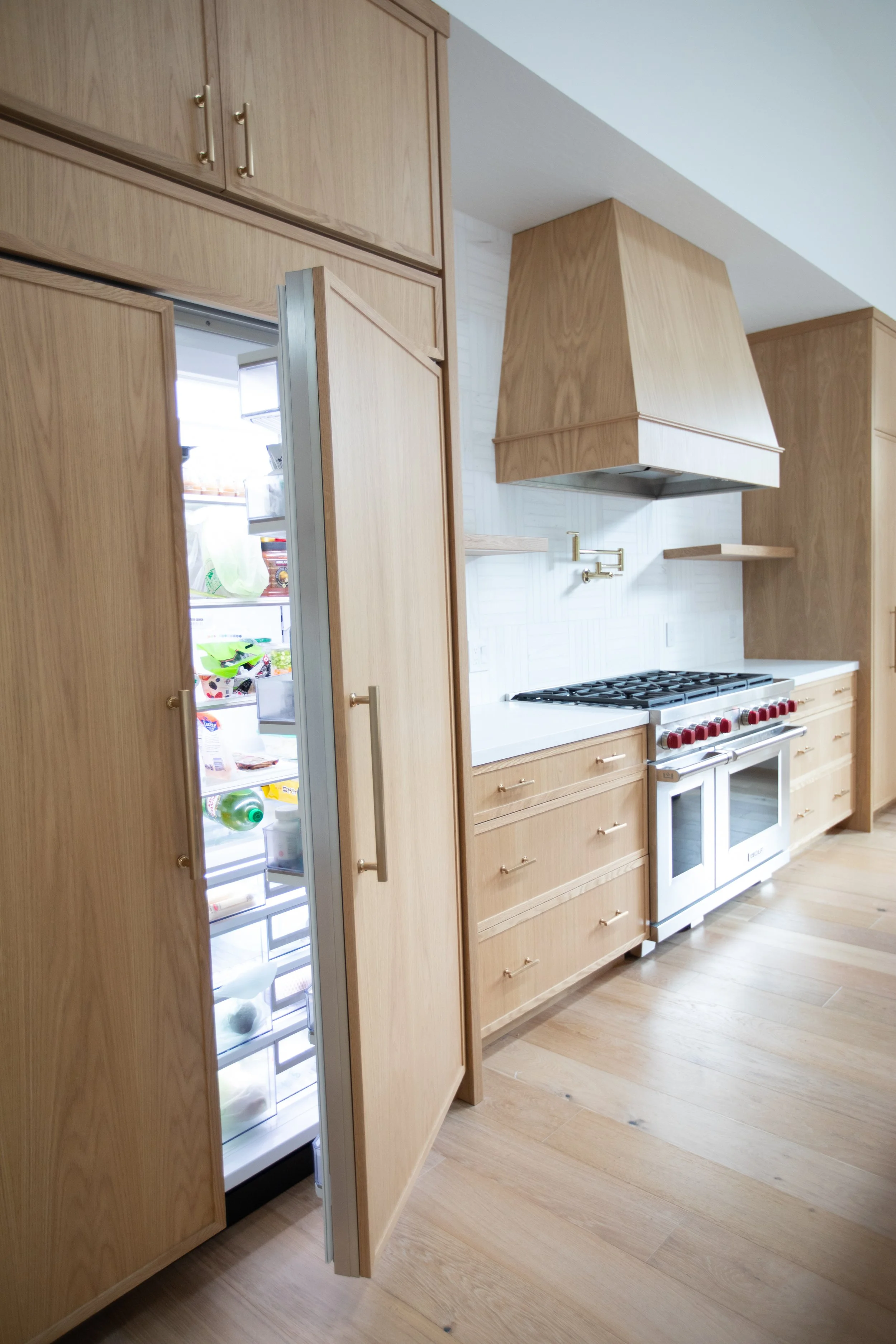 Kitchen with wood cabinets, a stainless steel refrigerator with the door open, a stove with red knobs, white countertops, and a white brick backsplash.