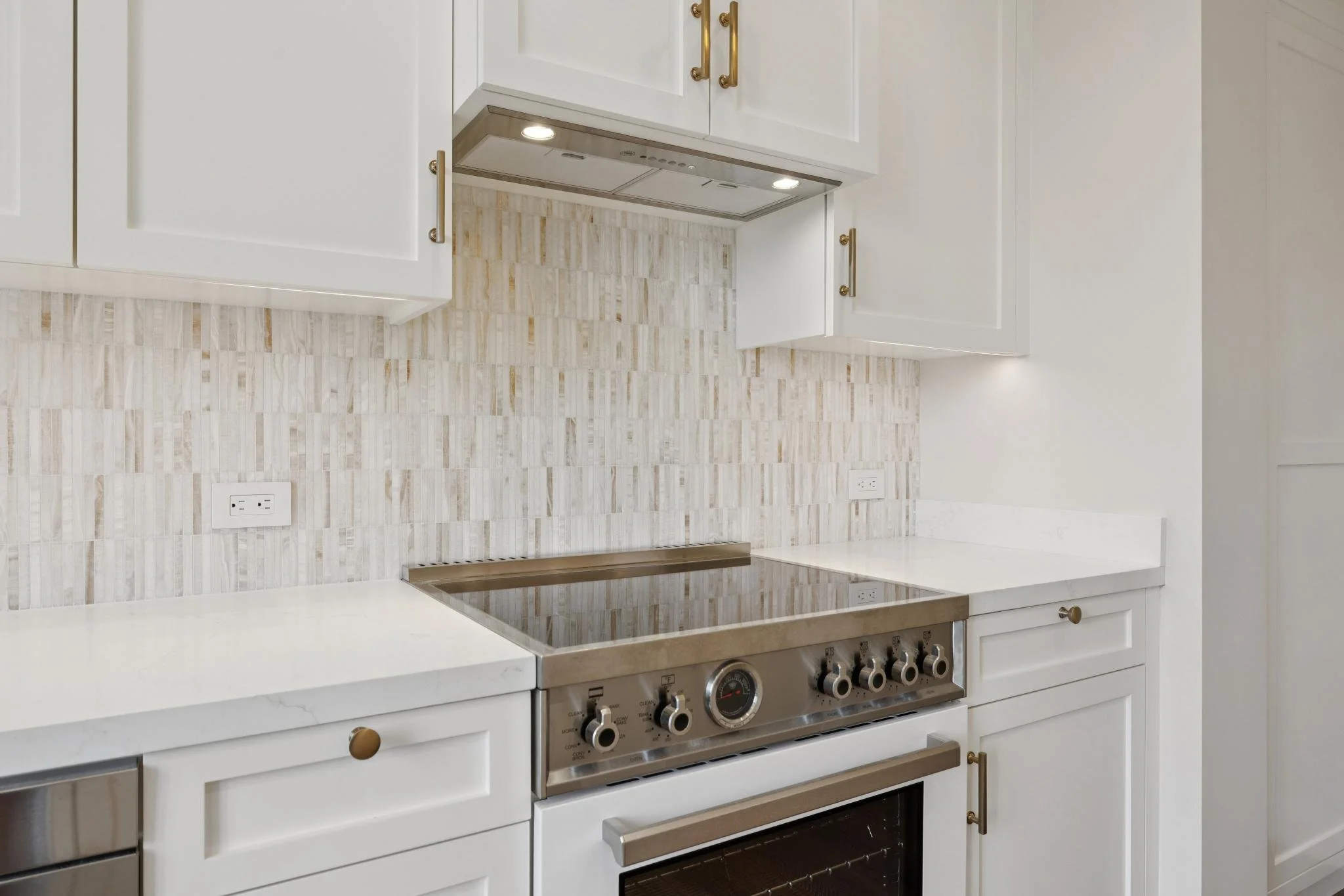 White kitchen with white cabinets, a beige backsplash, and stainless steel stove and oven.
