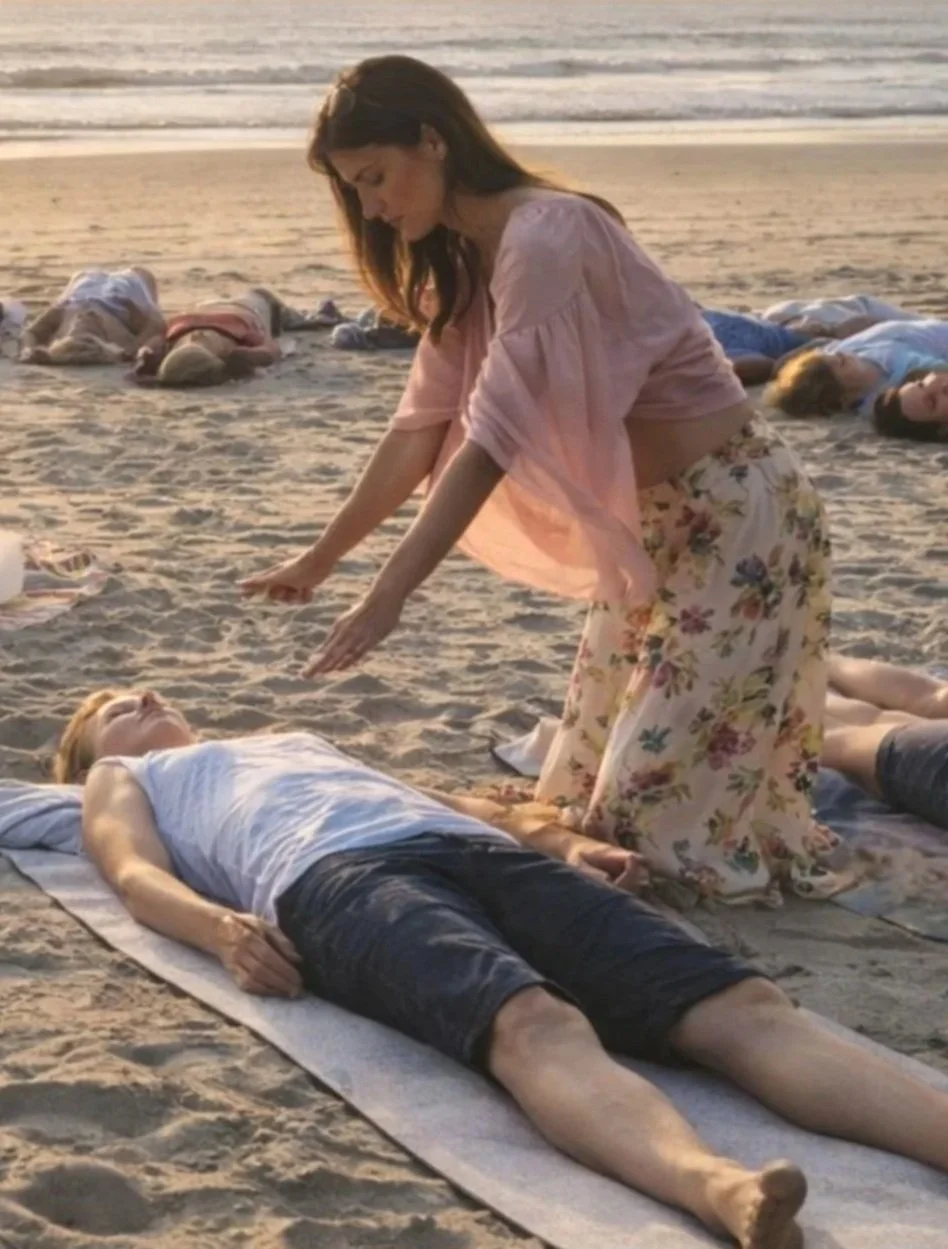 A woman practicing yoga on a beach during sunset, with multiple people lying down on the sand in the background.