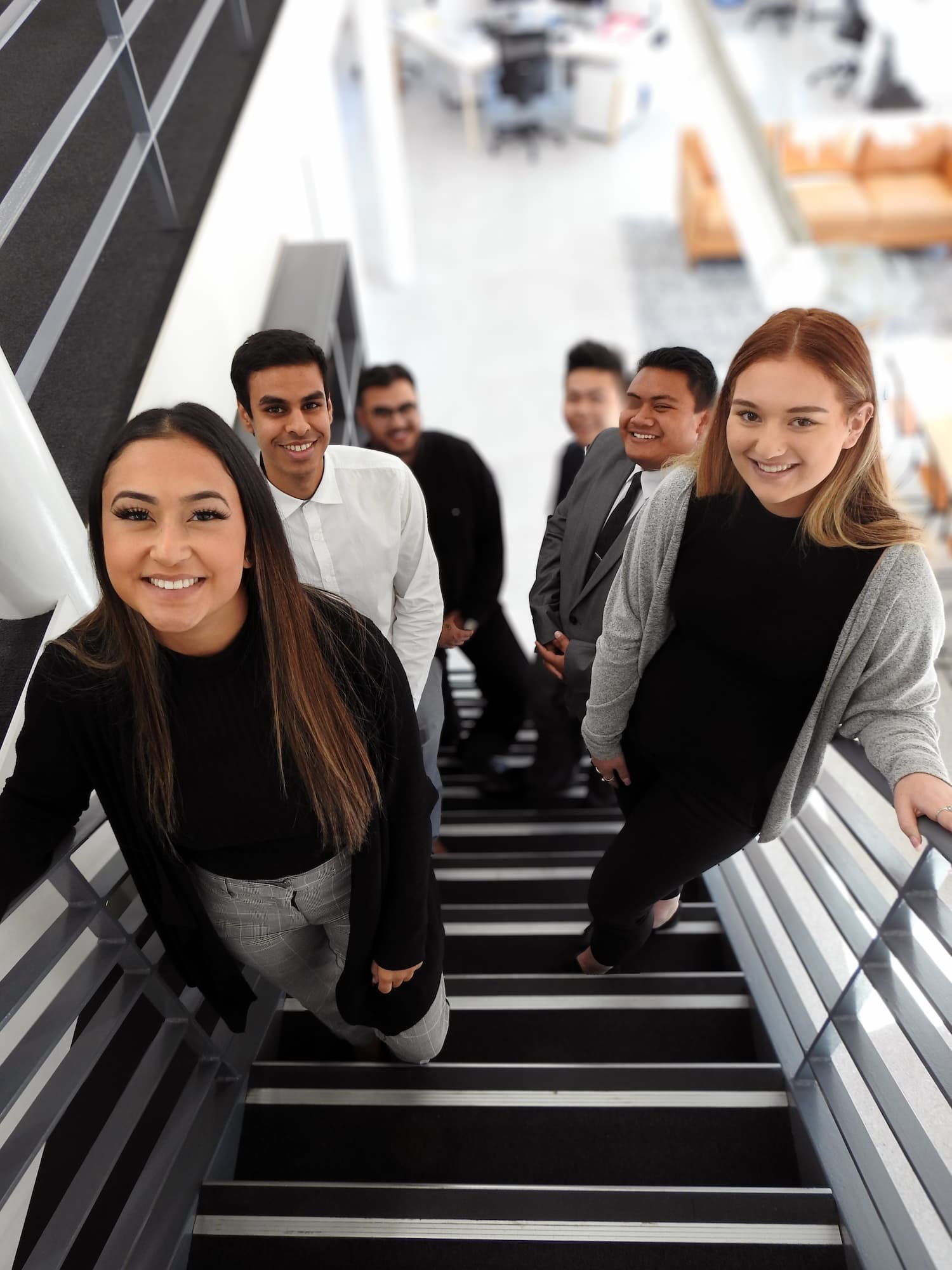 Group of young professionals standing on a staircase in an office environment, smiling at the camera.