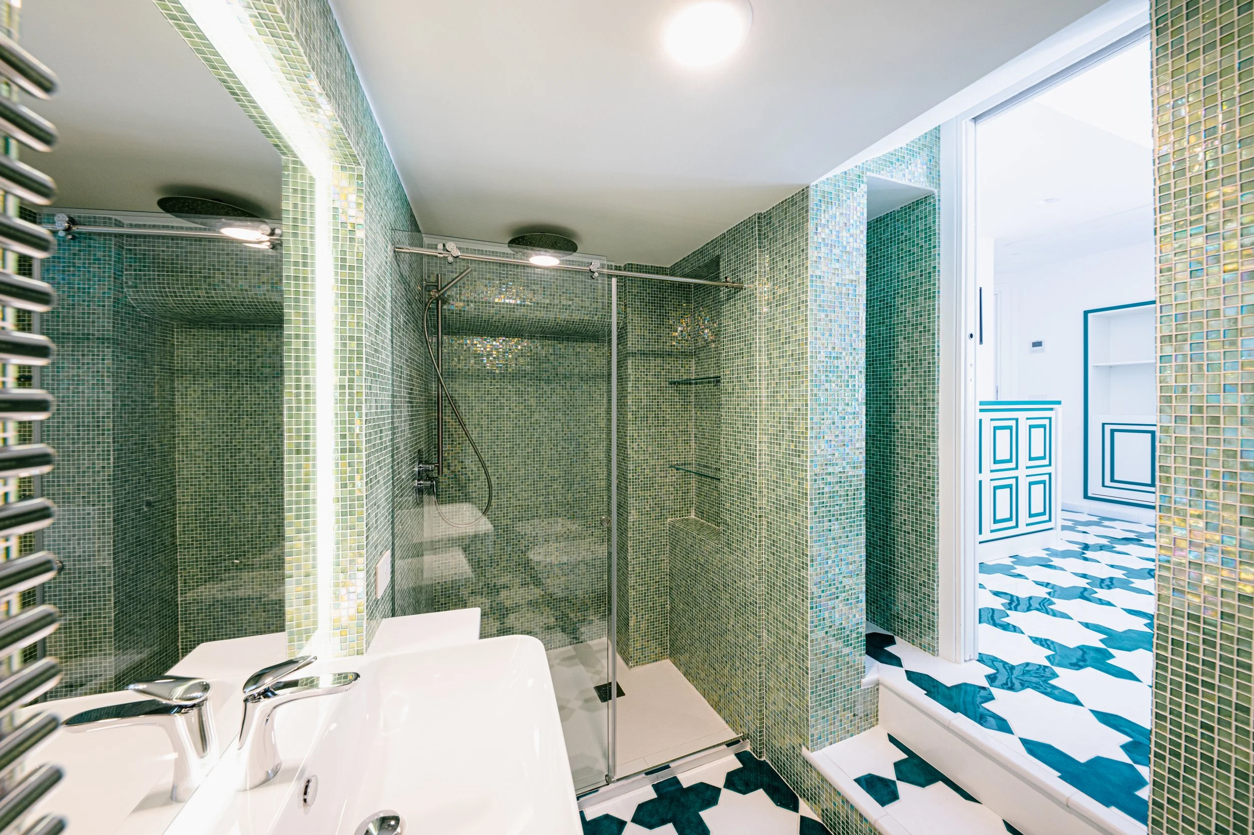 Green bathroom with big mirror, sink, and stand up shower ensuite to bedroom in Villa Marelda.