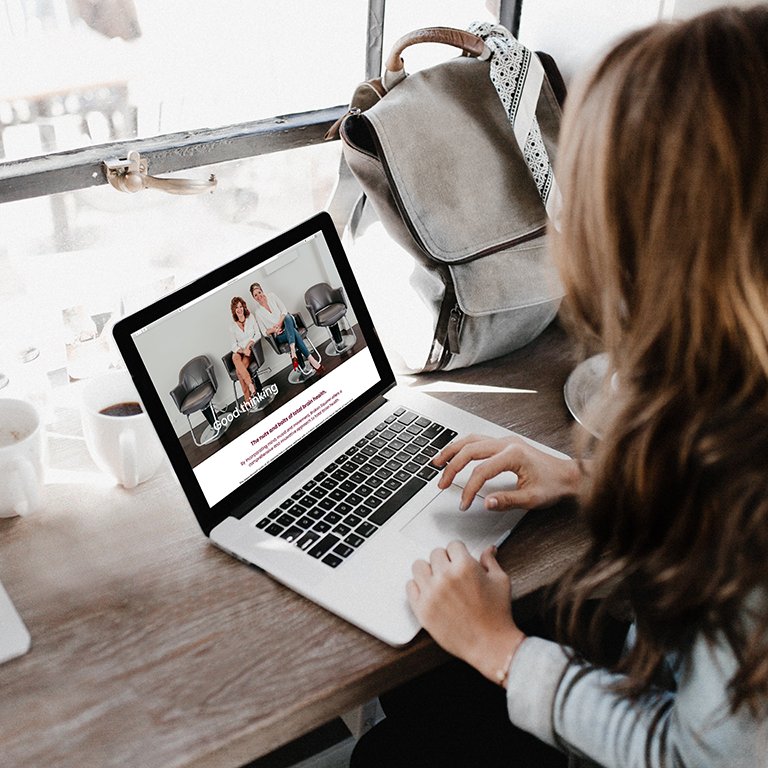 Person using a laptop in a café with a backpack and coffee cup on the table.