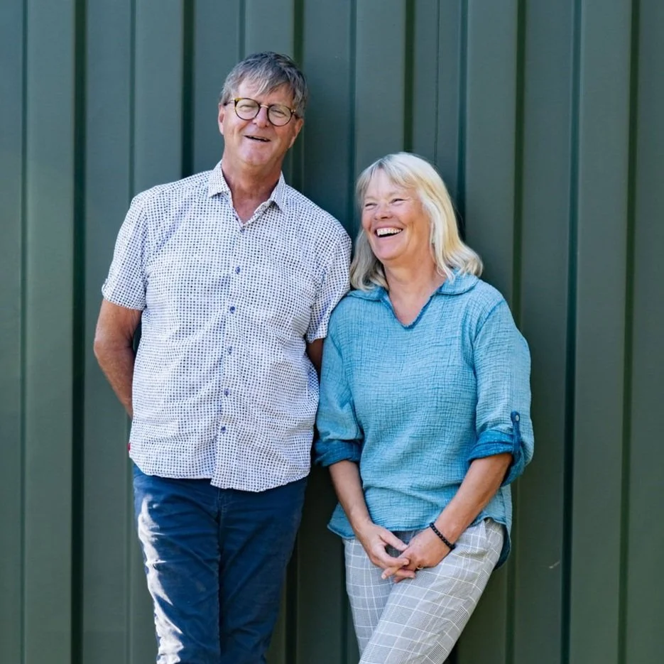 A man and a woman standing and smiling in front of a green wall.
