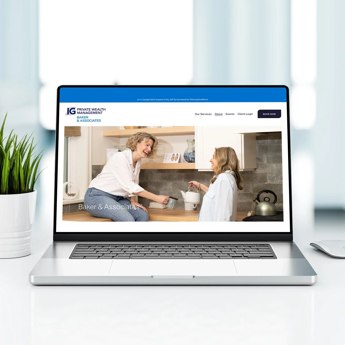 Laptop on a white desk displaying a webpage for Baker & Associates, a wealth management firm, with a picture of two women smiling and interacting in a kitchen.