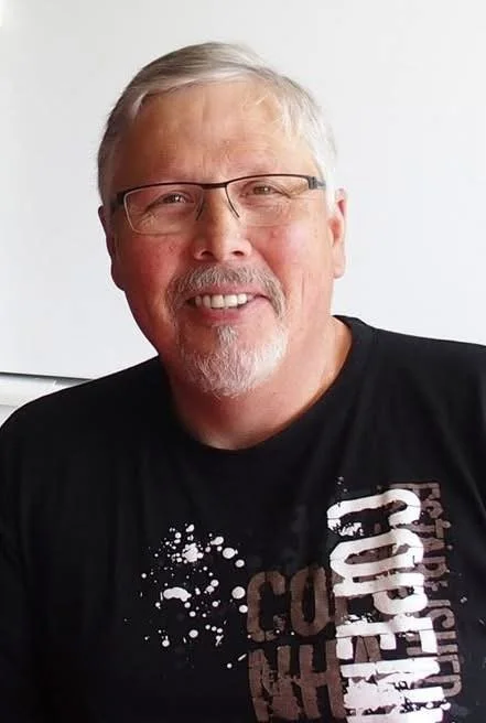 Al Stelton has short grey hair and half-framed glasses.  He is smiling at the camera.