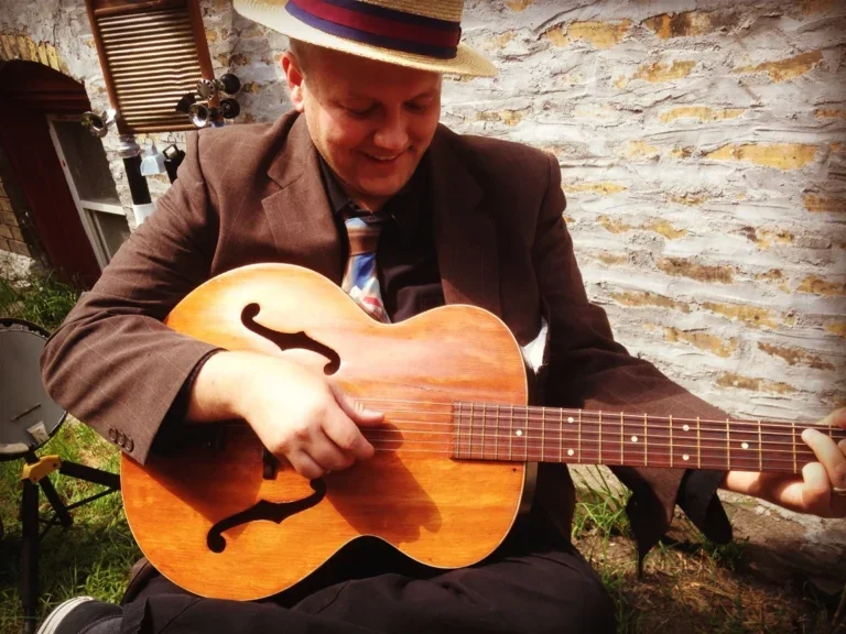 Jack Norton wears a fedora and strums his acoustic guitar