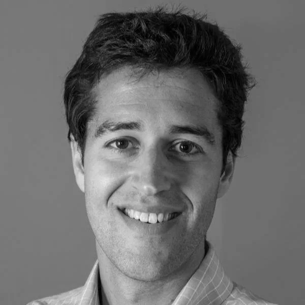 Black and white portrait of a smiling young man with short, dark hair, wearing a checkered shirt.