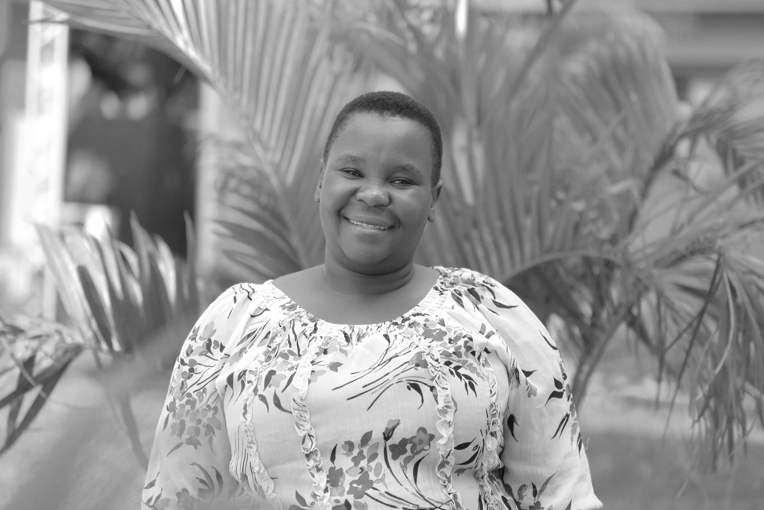 A smiling woman standing outdoors in front of large tropical plants.
