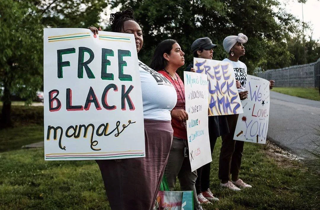 A photo of four people holding up signs saying “Free Black Mama’s” and “We Love You”.&nbsp;
