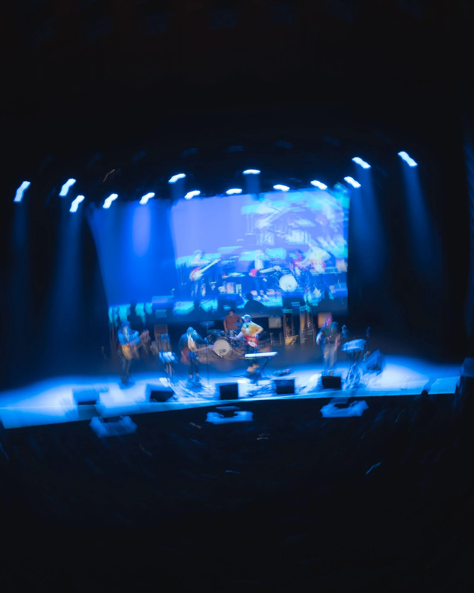 Blurred image of a stage with bright blue and white lights, and musicians performing.