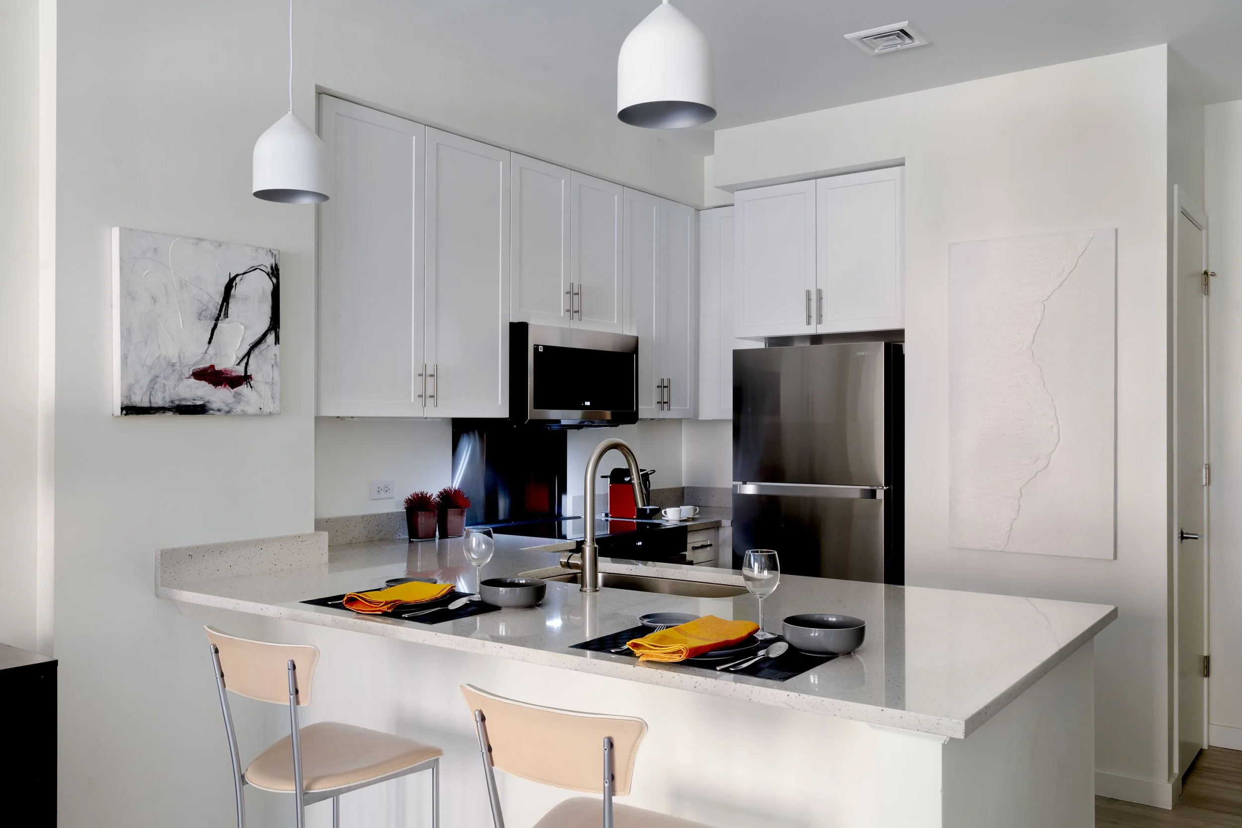 Modern kitchen with white cabinets, stainless steel refrigerator, and countertop with place settings, wine glasses, and napkins.