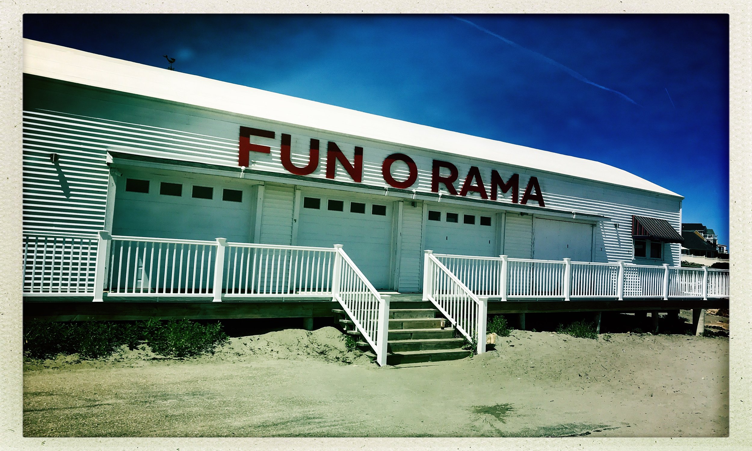 Building with "Fun-O-Rama" sign and white railing steps, under a clear blue sky.