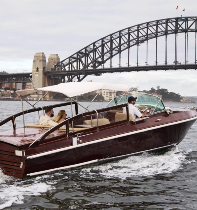 A motorboat with three people on a river, with a bridge in the background.