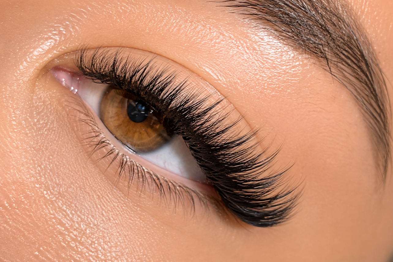 Close-up of a person's eye showing brown iris, long eyelashes, and smooth skin surrounding the eye.