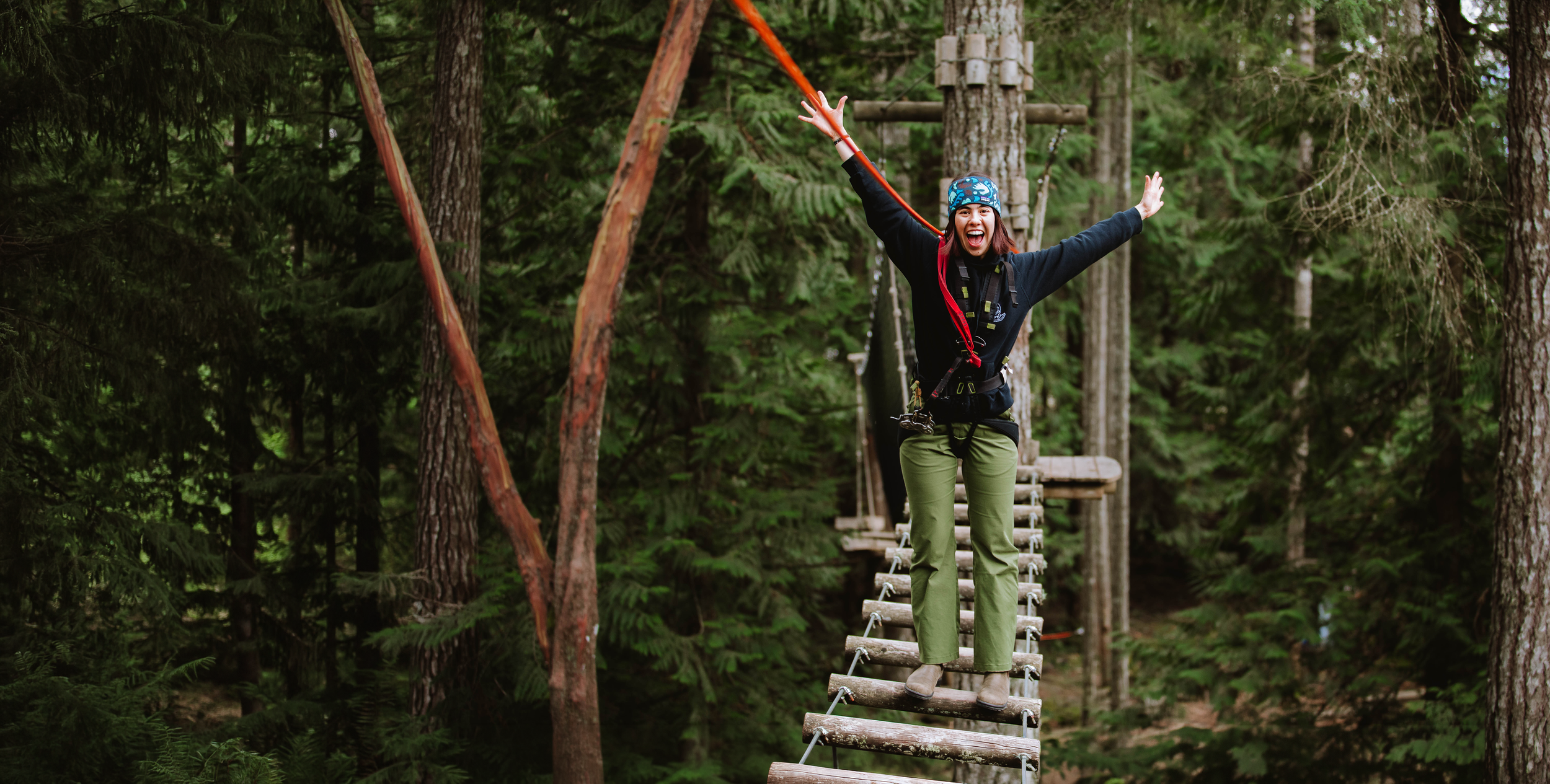 A WildPlay guest throwing her arms up on a suspension bridge