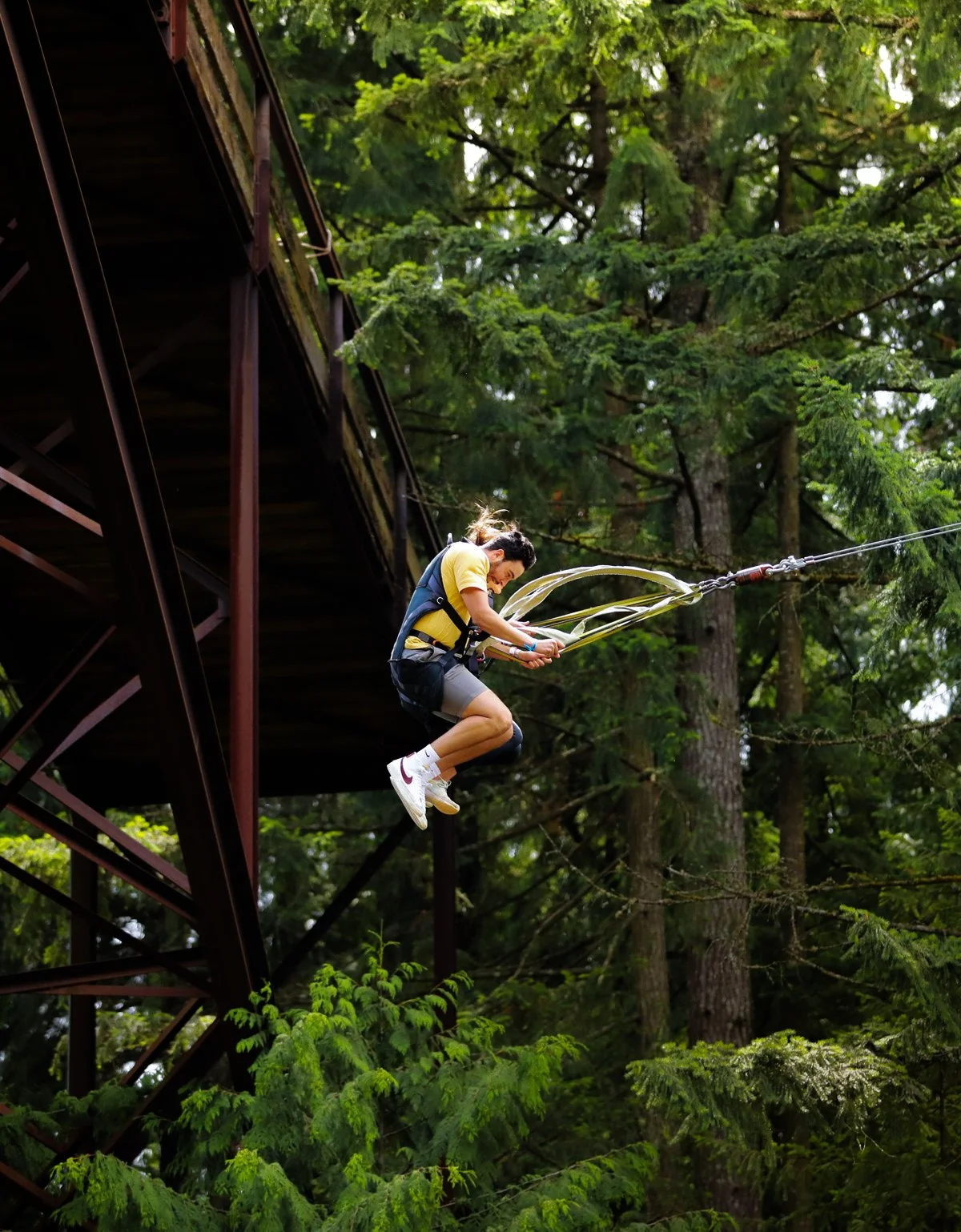 A person wearing a harness jumping off a platform into the forest, attached to a rope for bungee jumping.