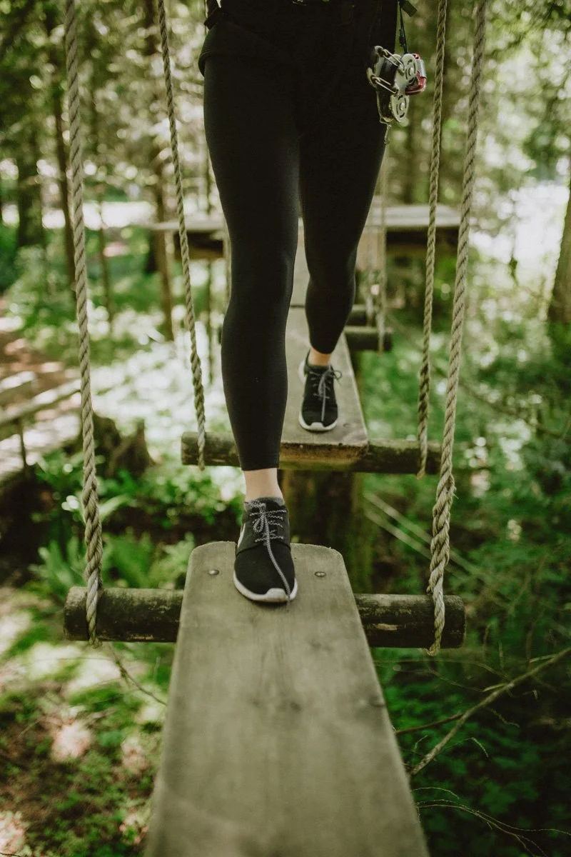 Person walking on a wooden suspension bridge in a forest.