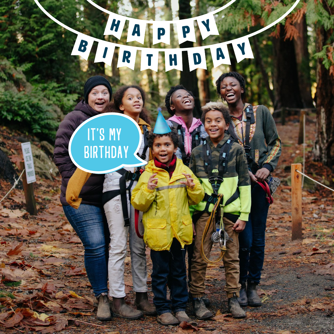 Three smiling individuals engaged in a tree-top adventure course, with safety harnesses on, pose on a wooden platform built around a tree. The lush green forest canopy forms a vibrant background, highlighting the adventurous outdoor activity.