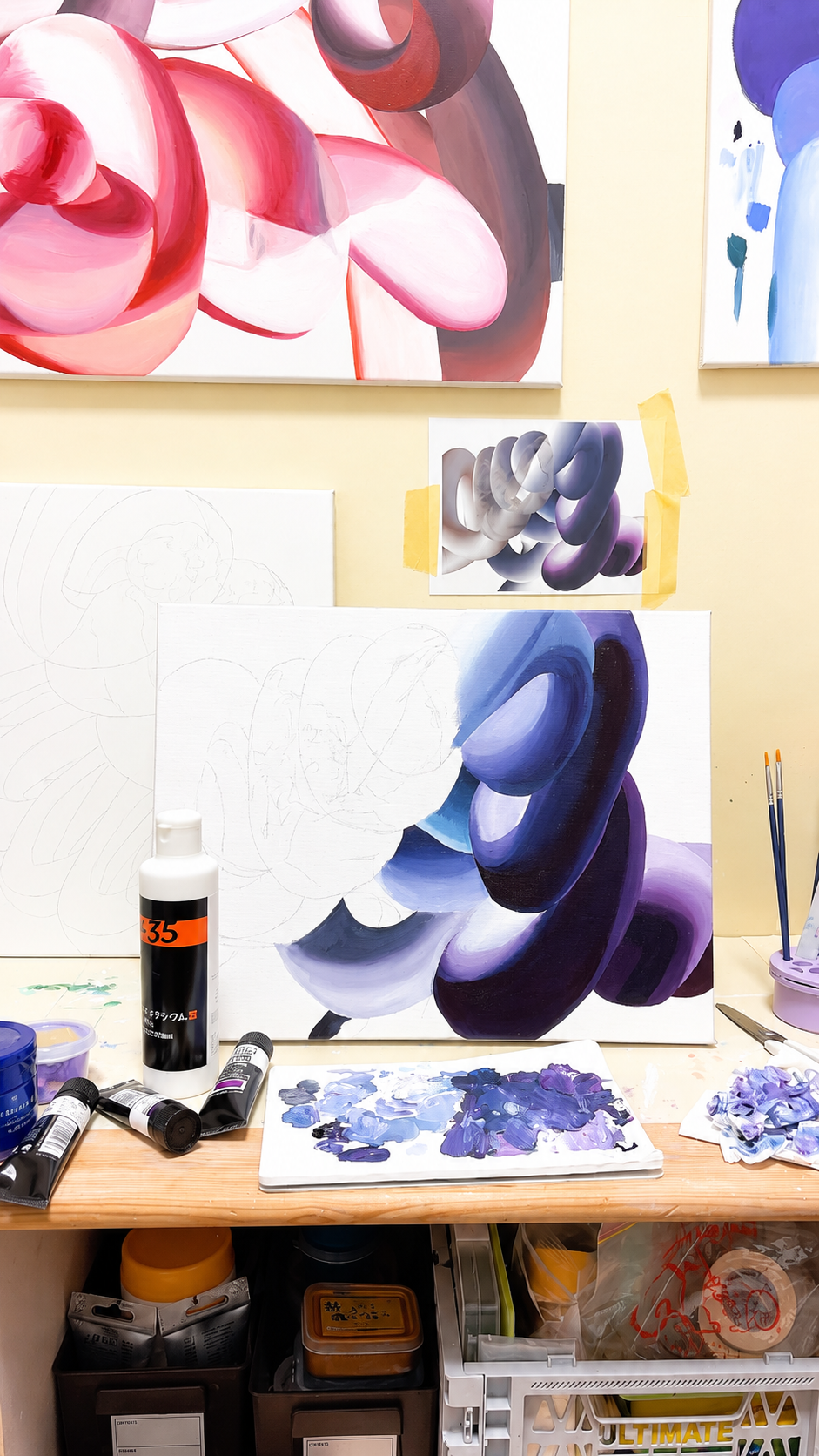 An artist's workspace with a partially completed abstract painting on a canvas, various jars of paint, brushes, and reference sketches and paintings pinned on the wall.