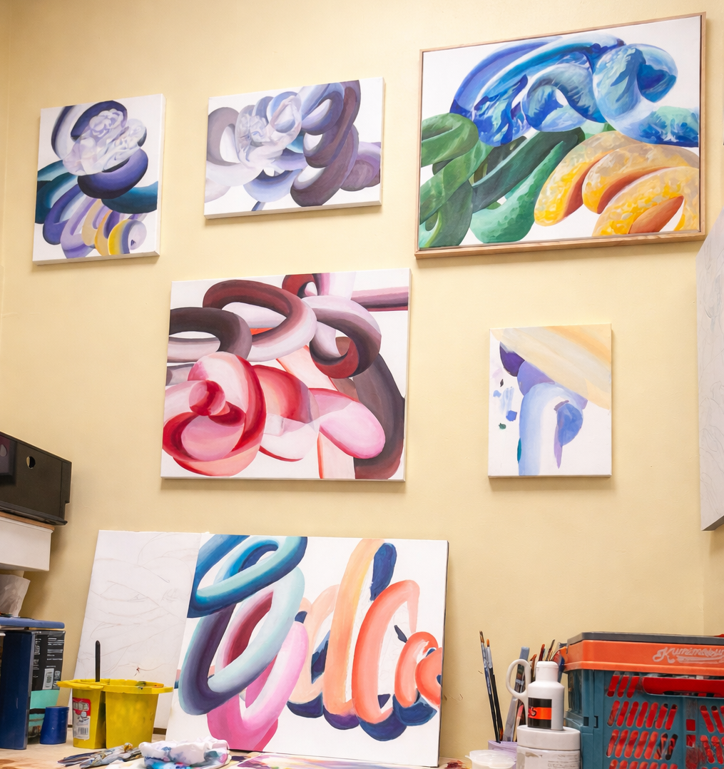 An art studio wall displaying multiple colorful abstract paintings with thick brush strokes, arranged in a collage style. Art supplies and equipment are visible at the bottom of the image.
