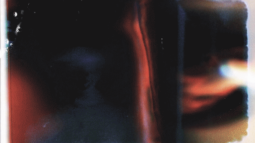 Close-up of a glossy, reflective surface with red and black coloring, possibly an electronic device or screen.