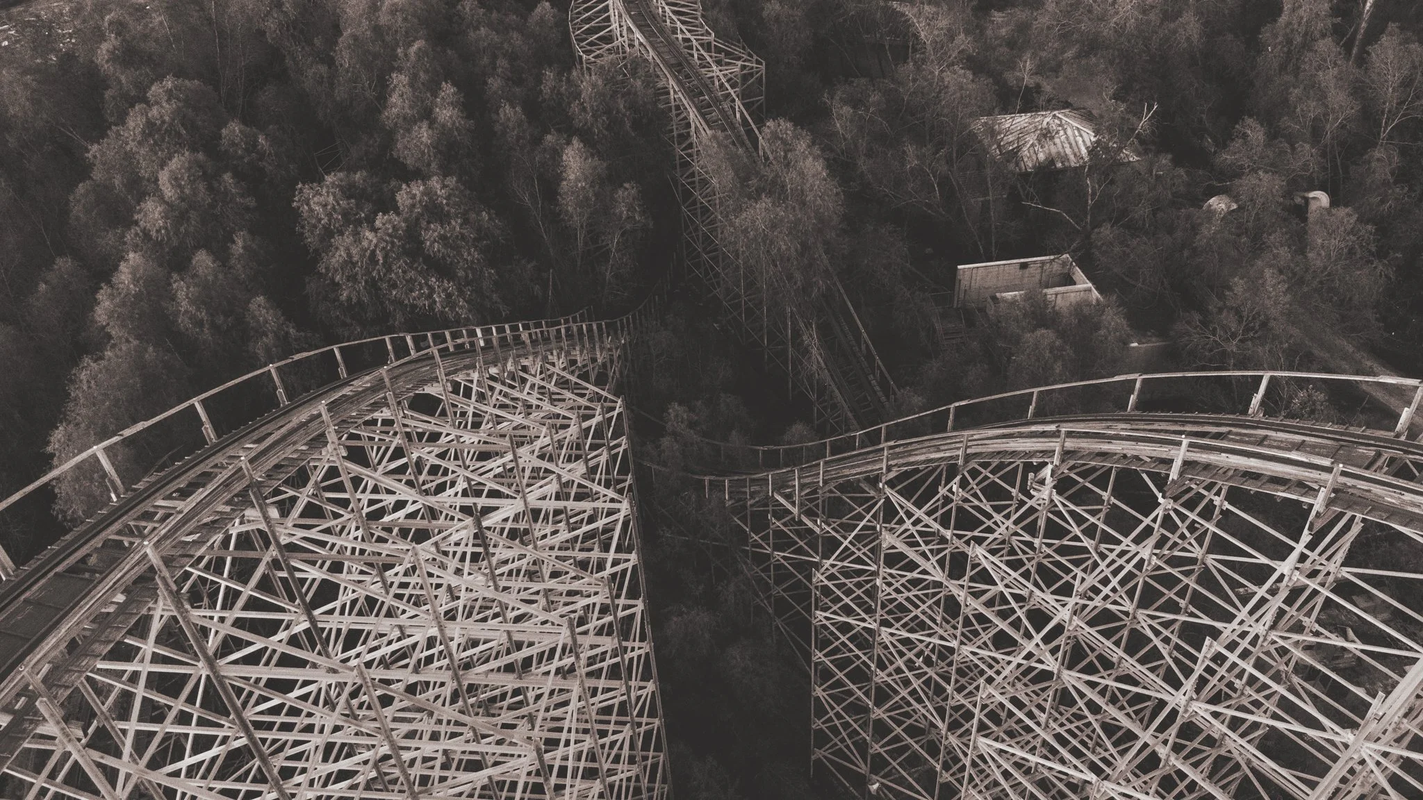Aerial view of a steel roller coaster track winding through a wooded area.