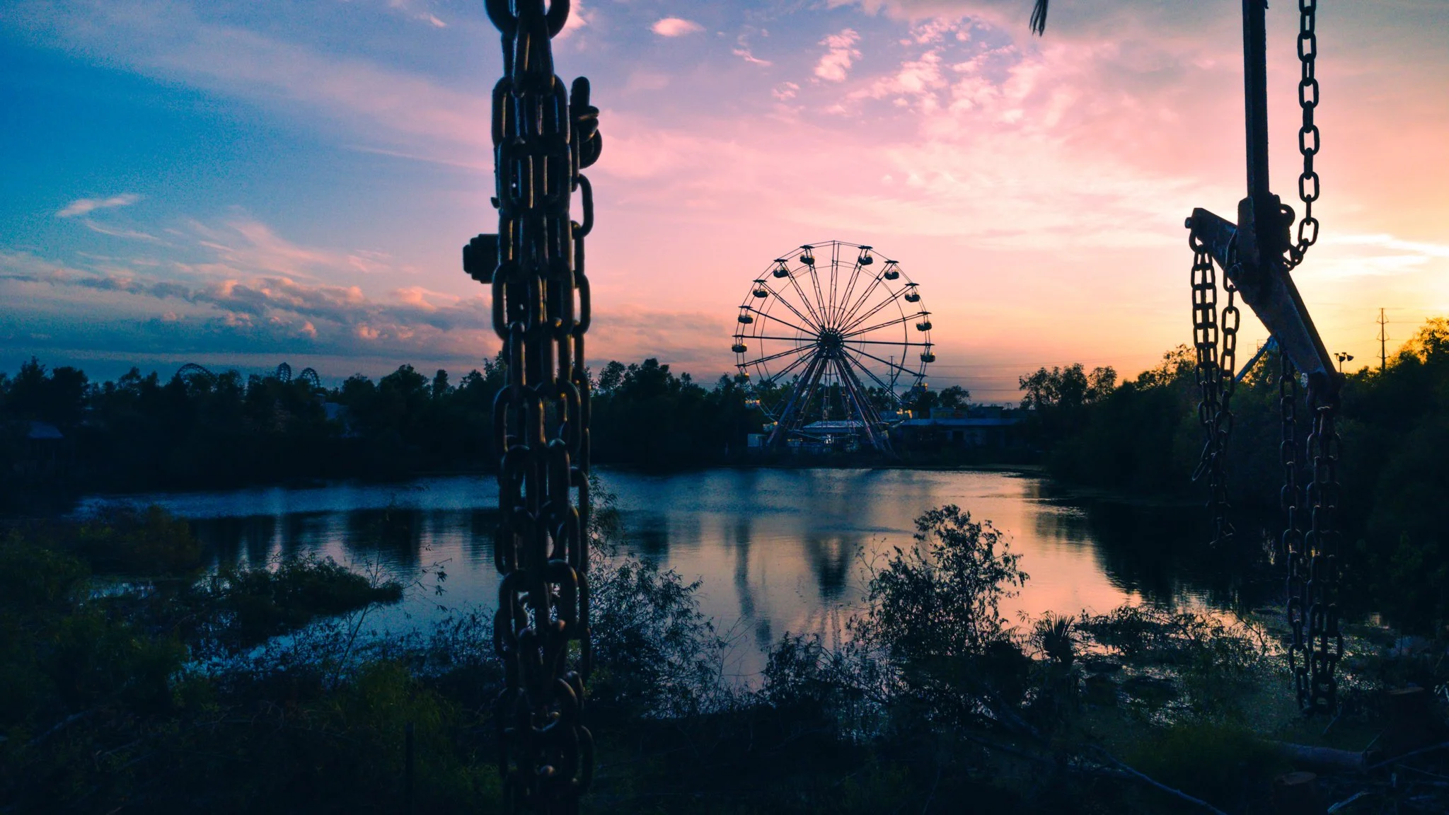 Sunset over a river with a Ferris wheel in the distance, seen through rusted chains of an abandoned swing set. the abandoned Six Flags New Orleans Jazzland. This iconic, world-famous park was devastated along with the city of New Orleans in 2005.