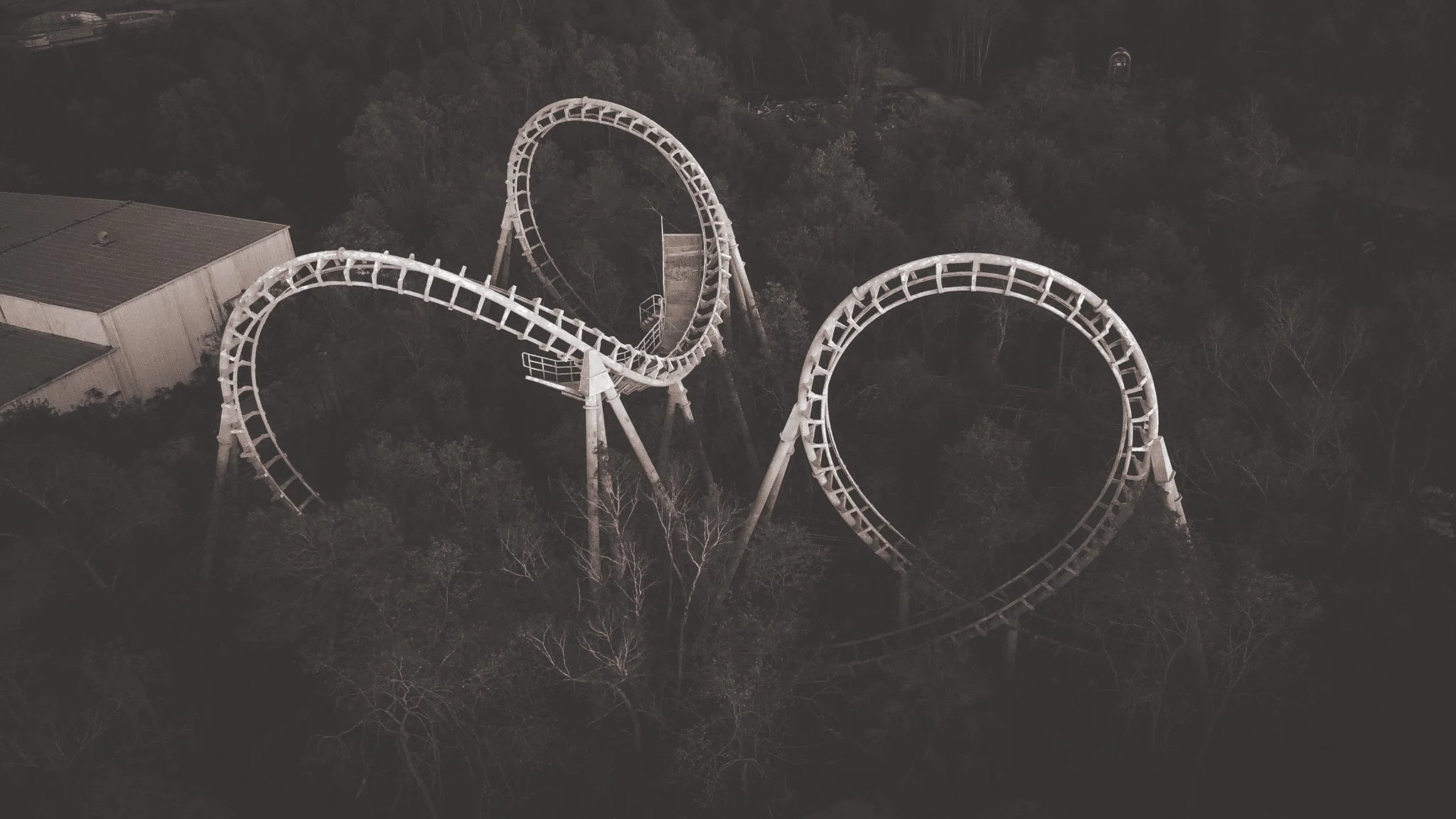 An aerial night view of the Zydeco Scream with a looping track surrounded by trees and a building nearby. the abandoned Six Flags New Orleans Jazzland. This iconic, world-famous park was devastated along with the city of New Orleans during Katrina.