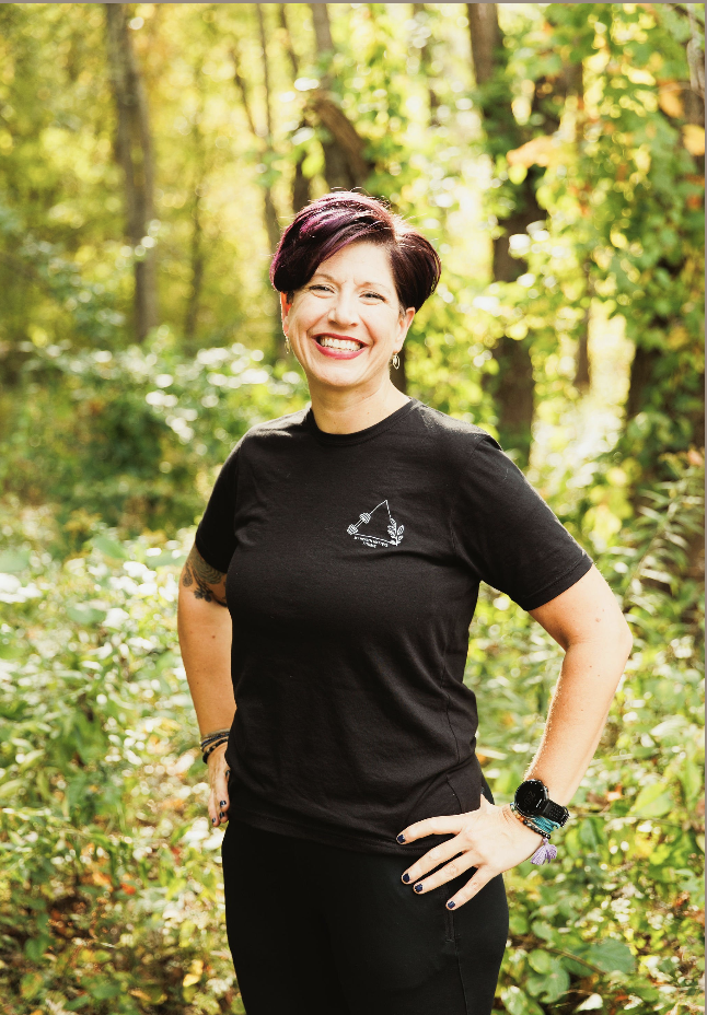 A woman with short hair standing and smiling in the forest in an My Health Matters t-shirt