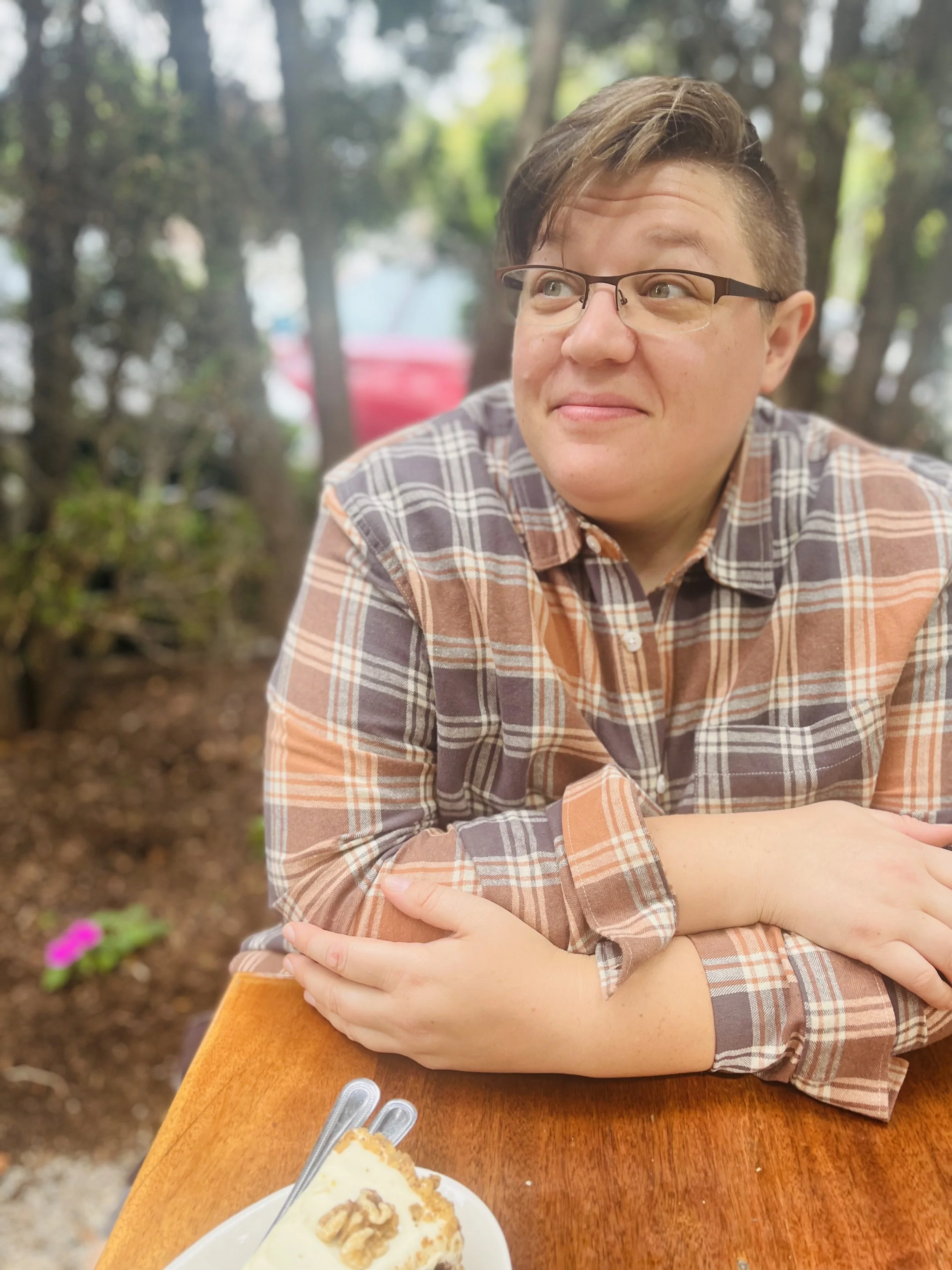 A person with short hair sitting and smiling at a table with a plaid shirt on