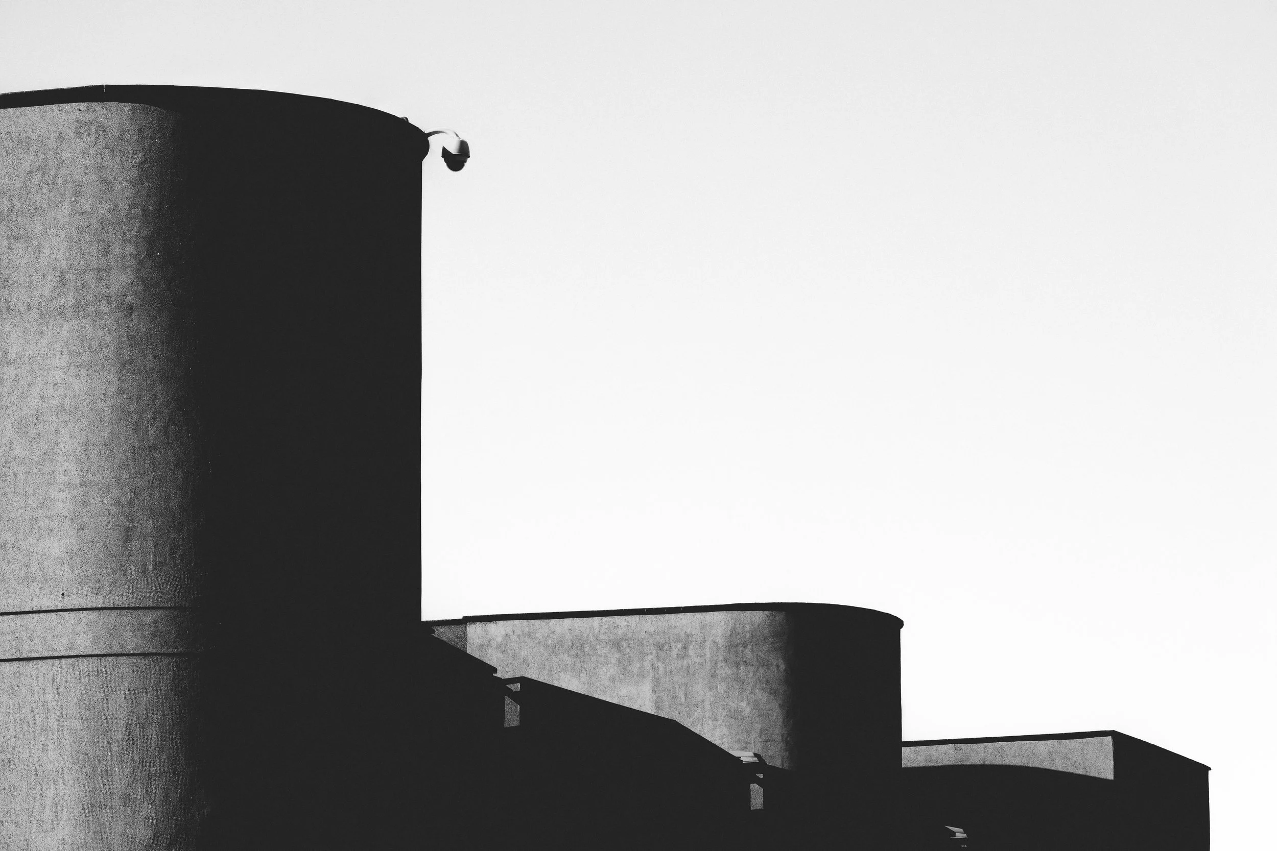 Black and white photograph of modern building with large, rounded concrete structures and a small security camera on top.