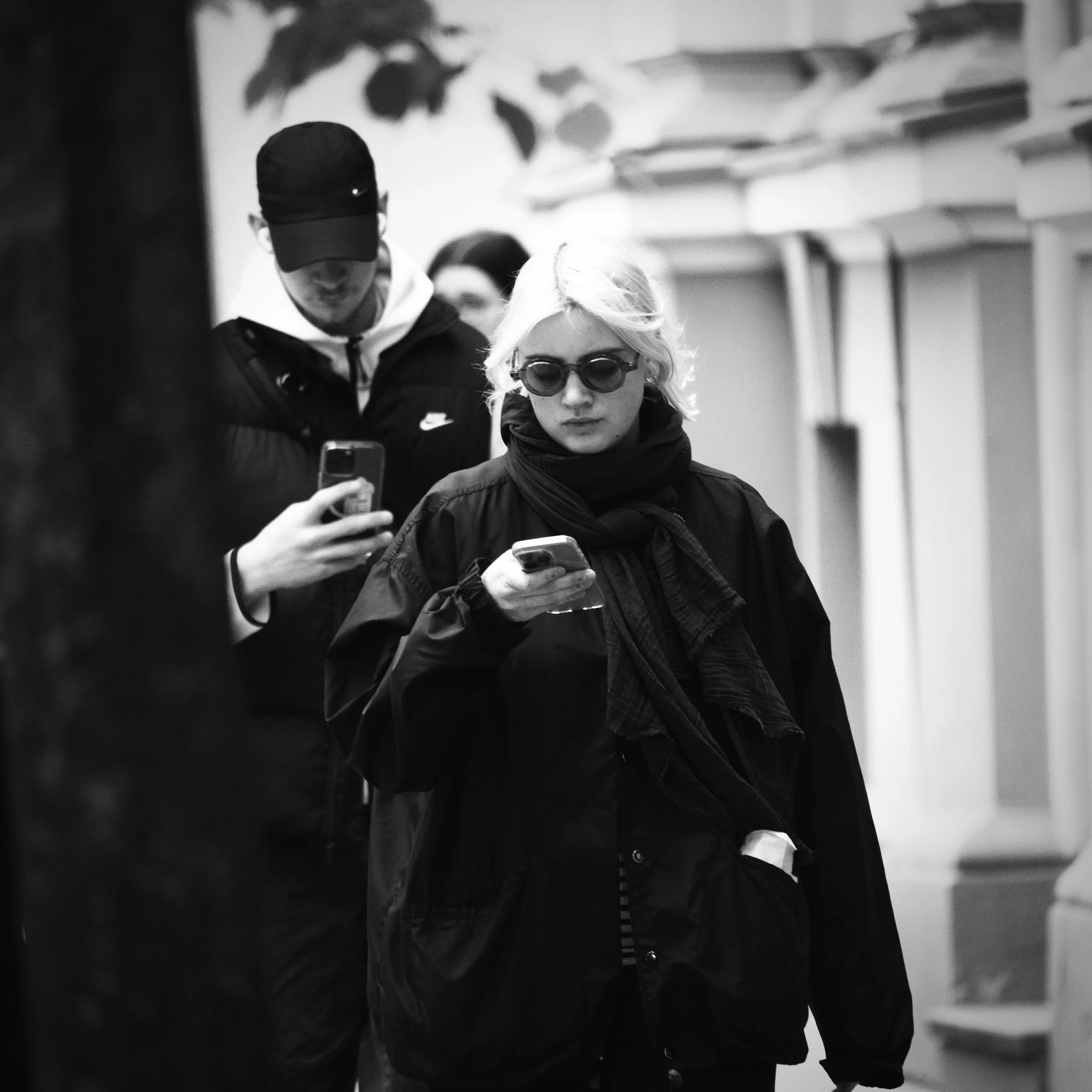 A black and white photo of three people looking at their phones in an urban setting.