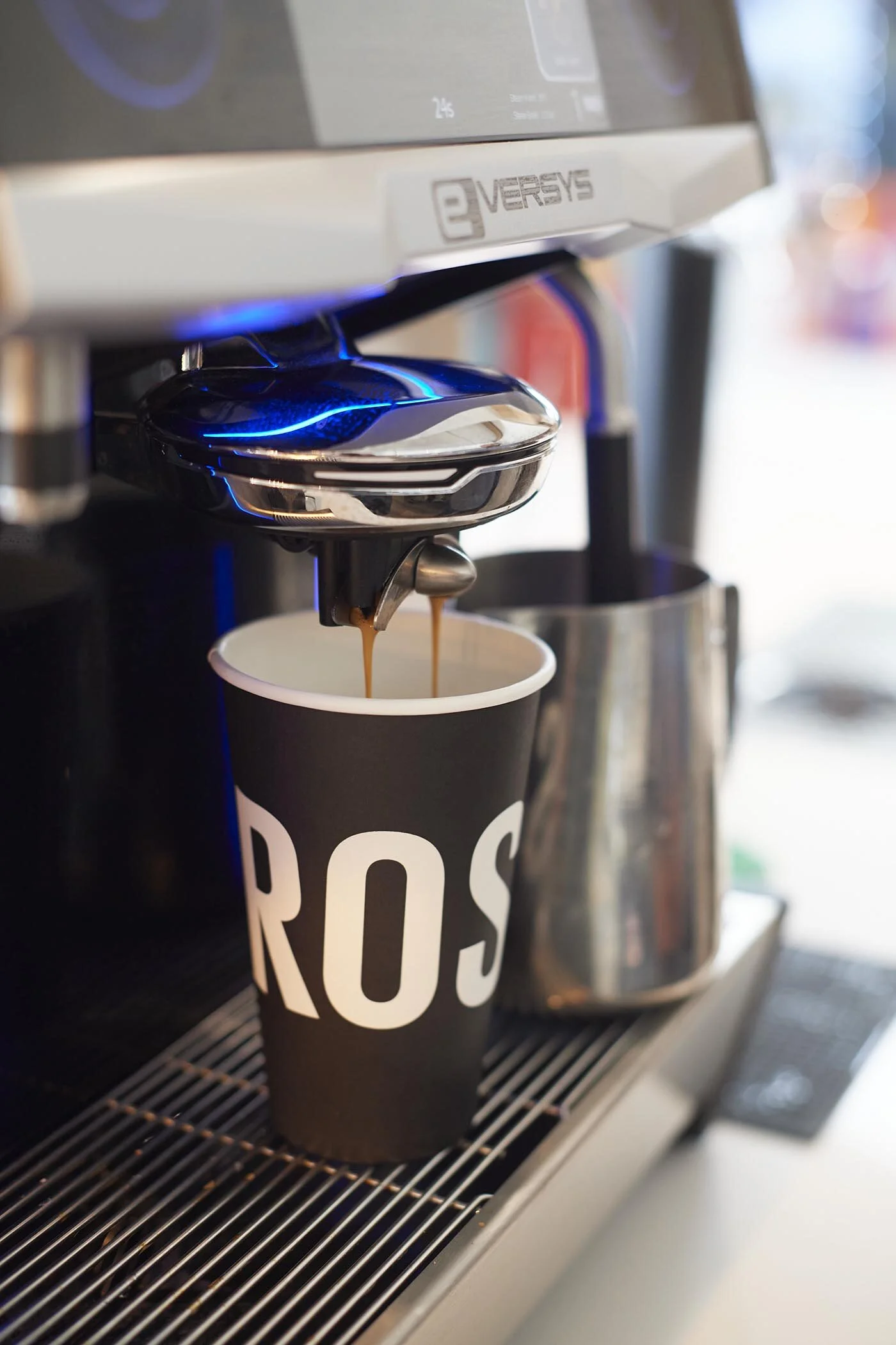 A coffee machine dispensing coffee into a black cup with white letters spelling 