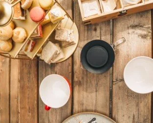 Top-down view of a wooden table with cheese, bread, and small containers, along with cups and bowls.