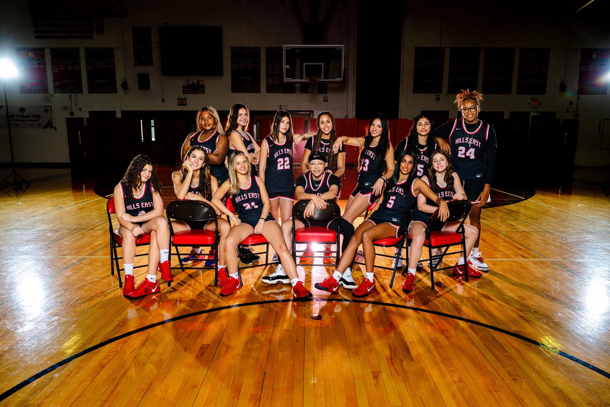 A girls' basketball team in their uniform posing for a team photo inside a gymnasium with a basketball hoop in the background.