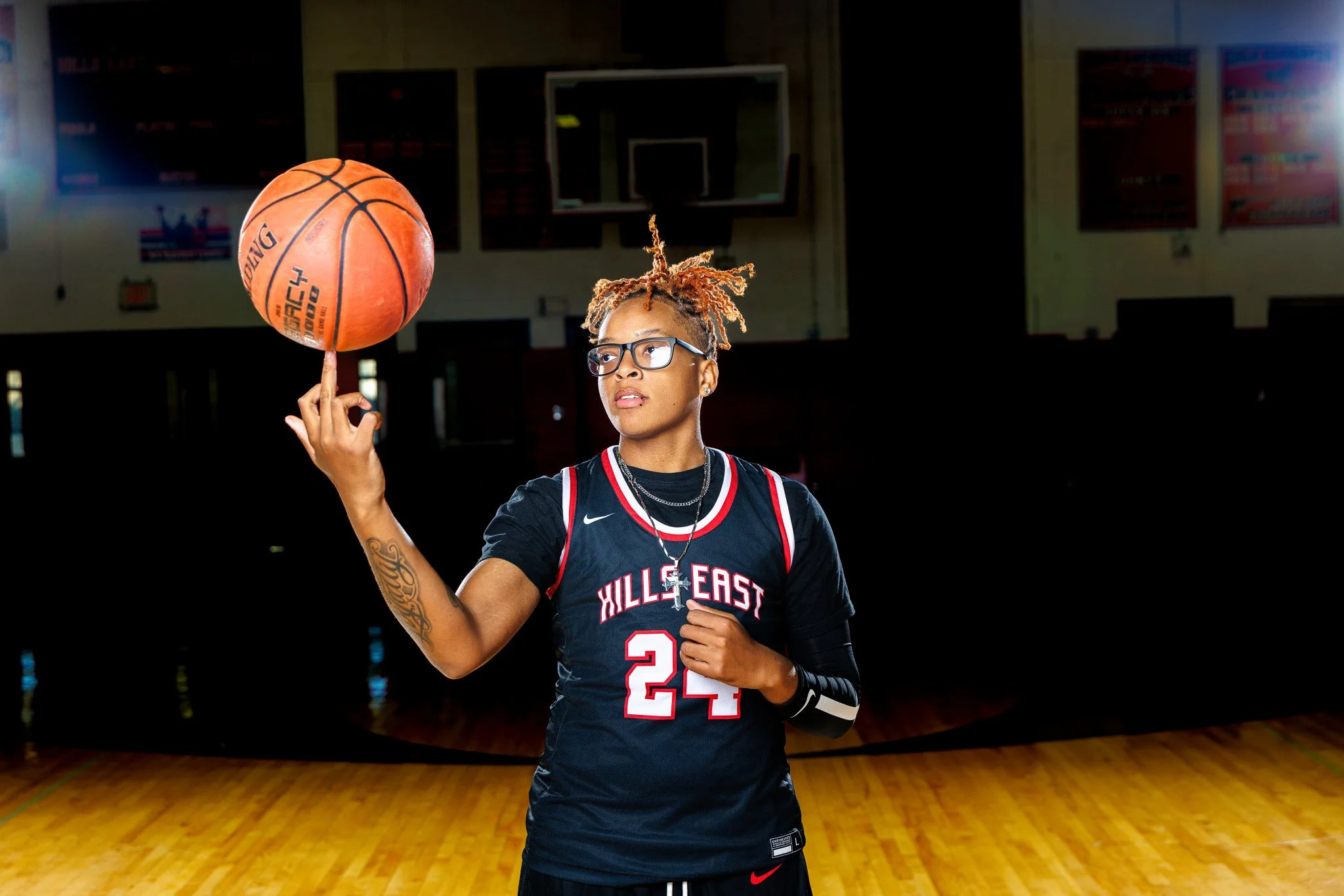 A female basketball player in a black jersey with red and white accents, number 24, spinning a basketball on her finger inside a gymnasium.