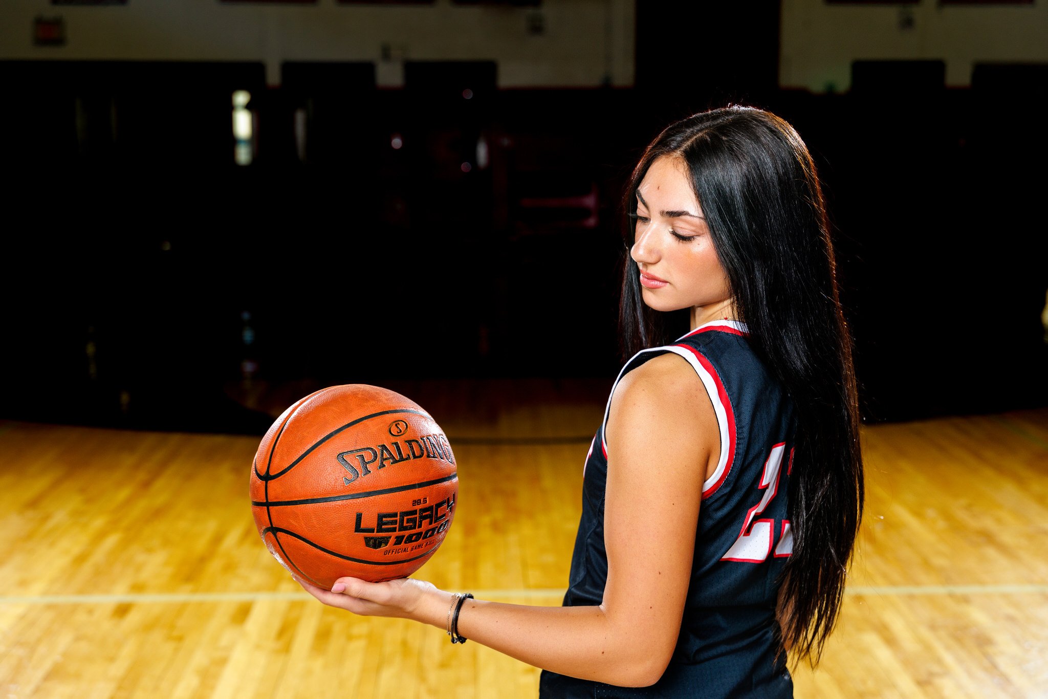 Young woman in basketball jersey holding a basketball on an empty court