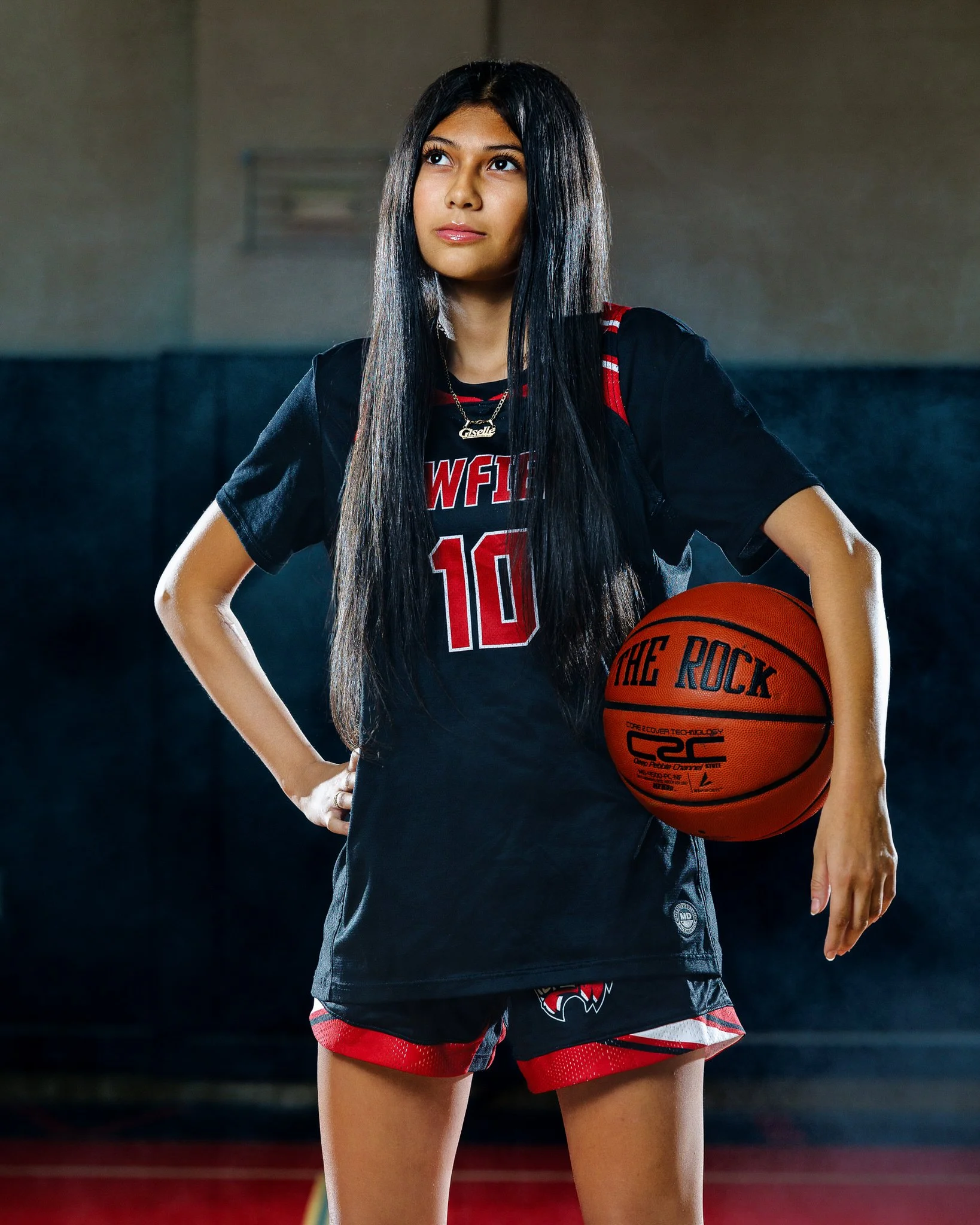 Young woman in a basketball uniform holding a basketball on a basketball court.