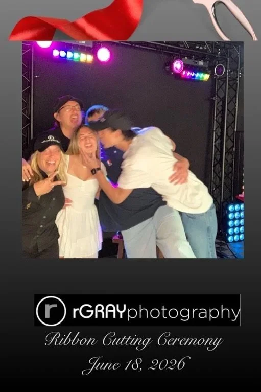 Group of five people celebrating at a ribbon cutting ceremony with colorful stage lighting in the background. They are smiling and embracing each other, marking an event on June 18, 2026.
