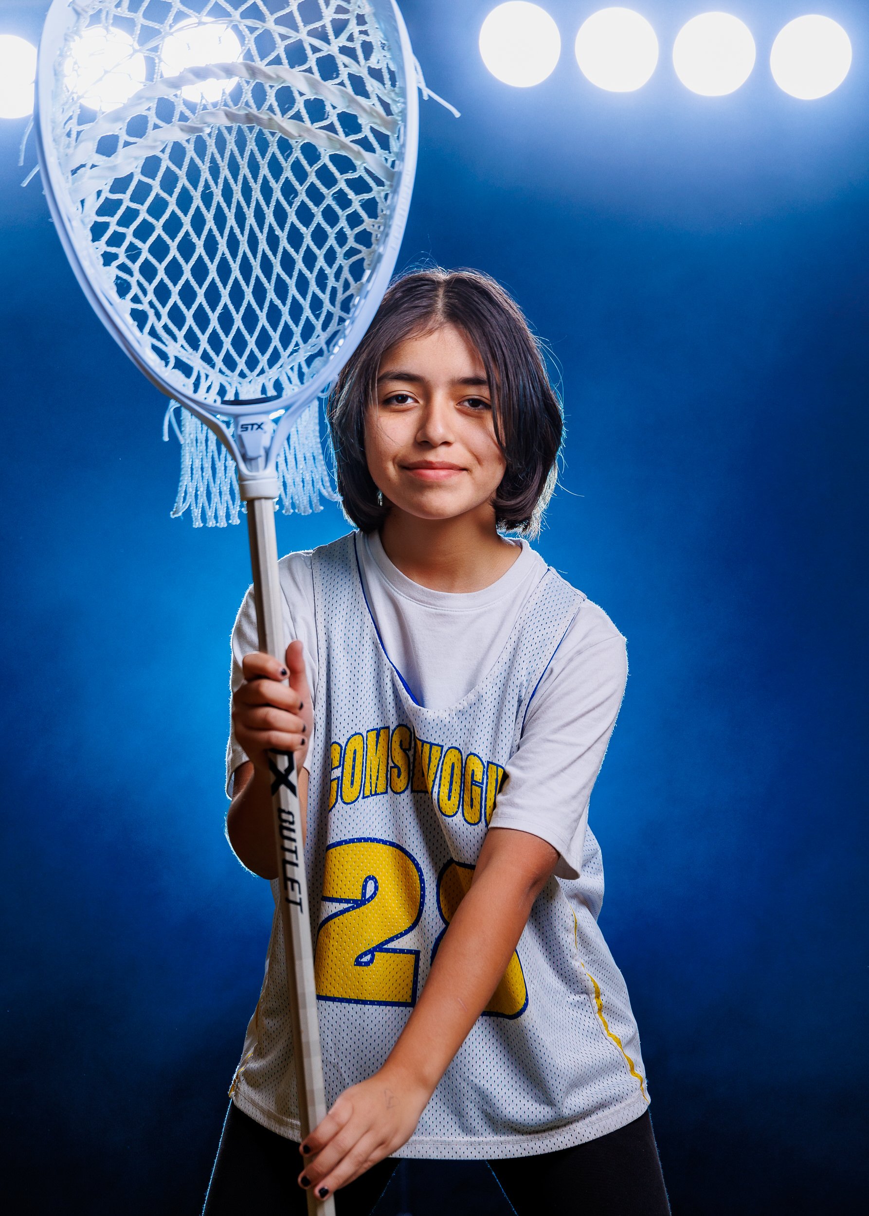 Youth lacrosse player holding a goalie stick under stadium lights.