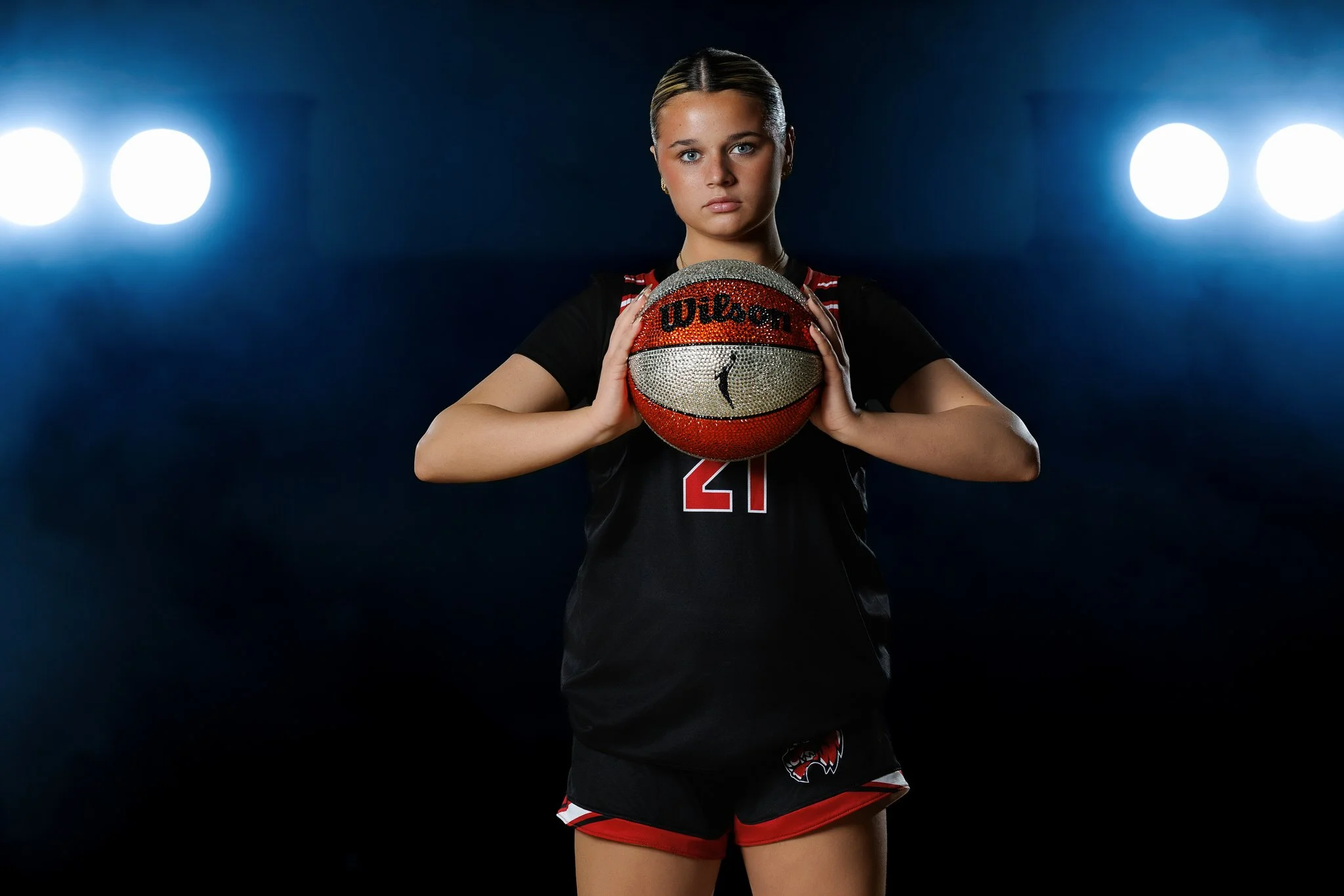 A female volleyball player holding a Wilson basketball in front of a dark background with two bright lights.