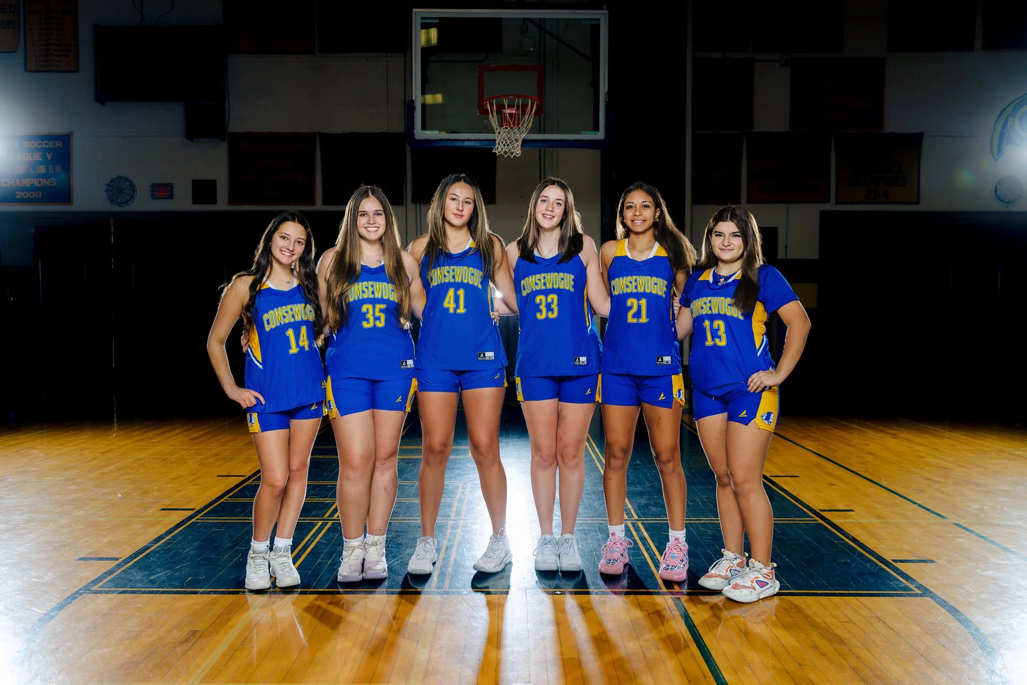 Six young female basketball players in blue and yellow Team Consewogue uniforms standing on a basketball court with a hoop in the background.
