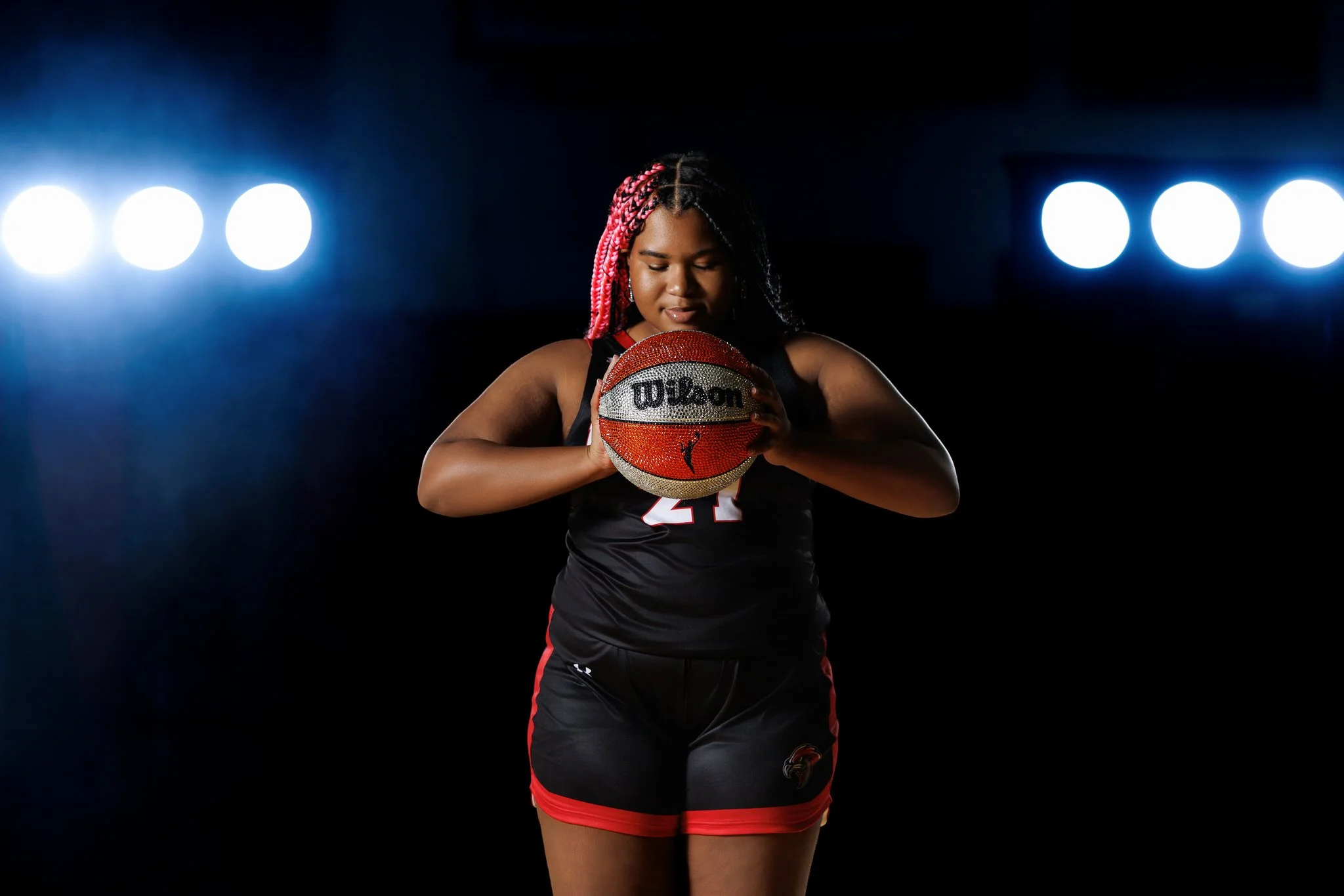 Female volleyball player holding a Wilson volleyball in a dark studio with bright lights in the background.