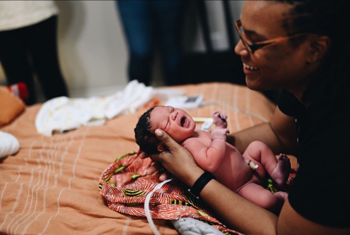 A newborn baby being held by a person on a bed, with a blanket underneath.