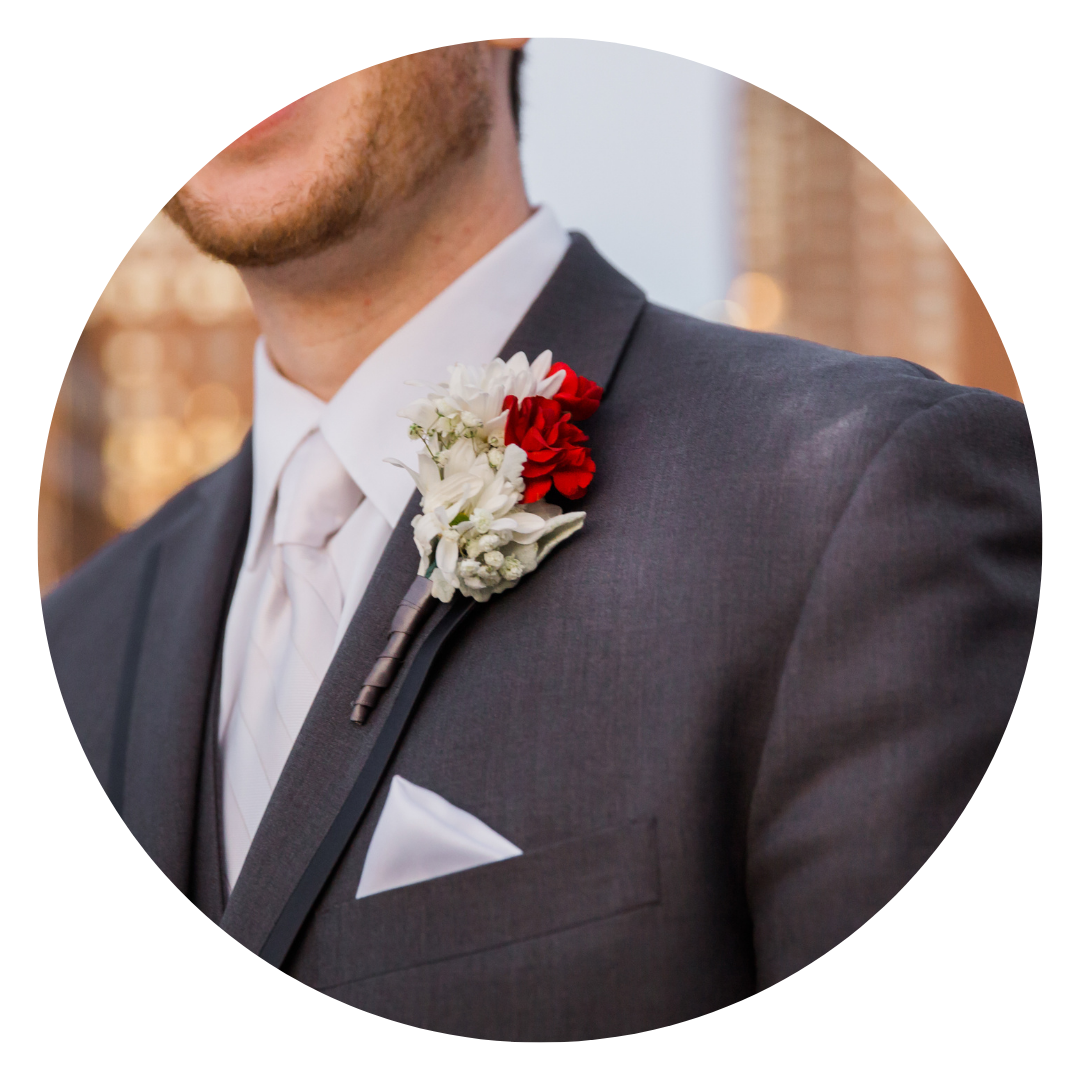 Close-up of a man in a dark gray suit with a boutonniere of white and red flowers on his lapel.