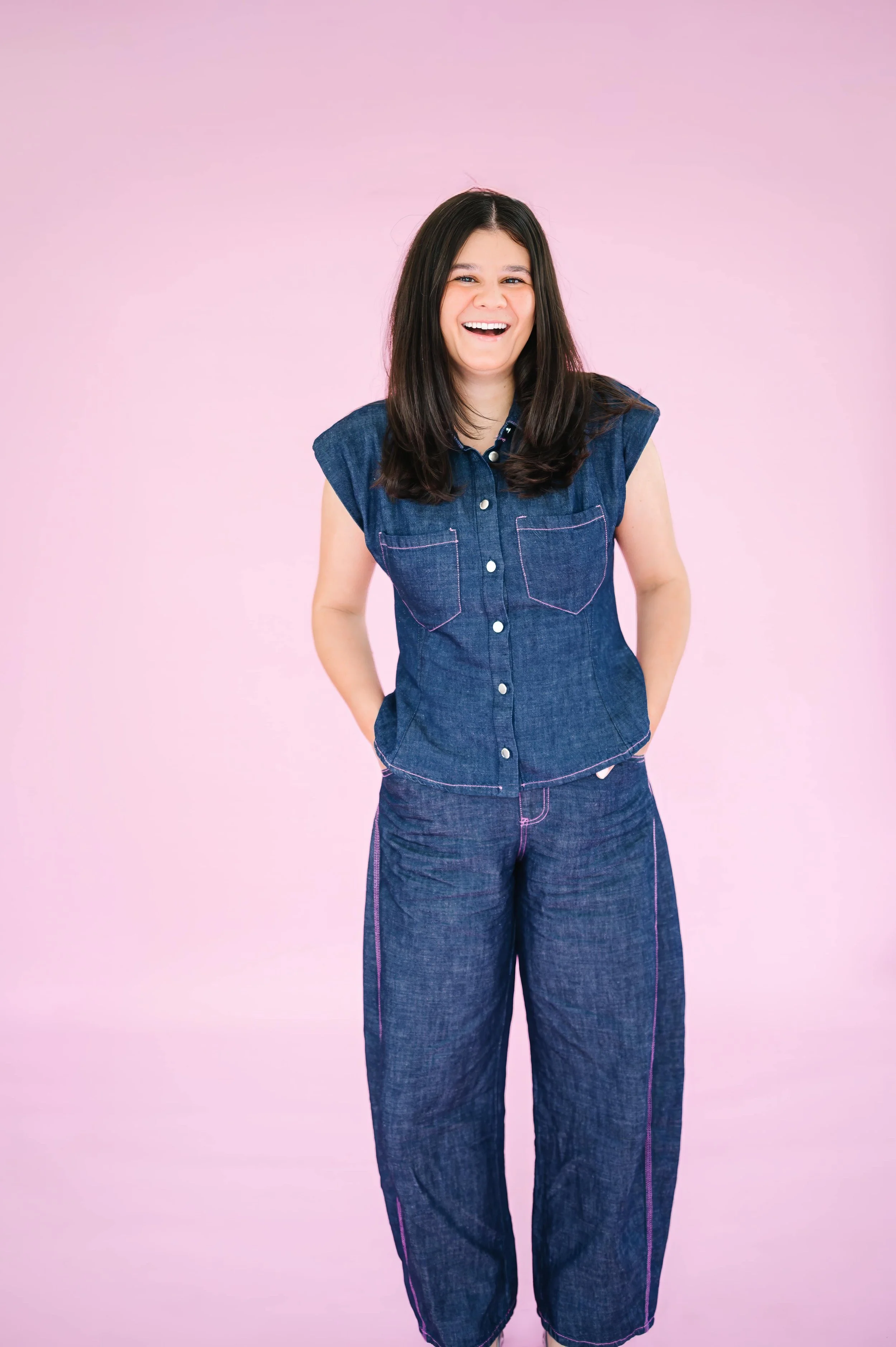 Annie Bradshaw standing with her hands in the pockets of a denim jumper against a pink background for Pep & Party Co. branding.