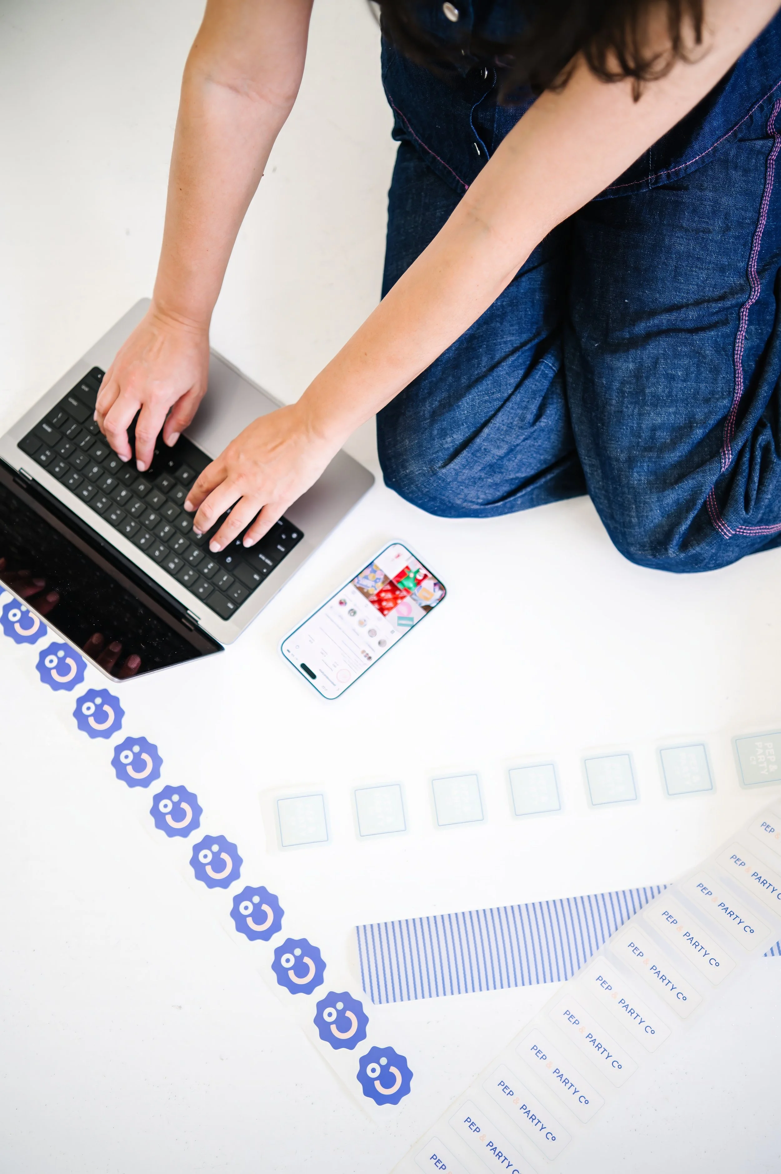 Annie Bradshaw working on a computer surrounded by custom stickers while creating corporate gift boxes for Pep & Party Co.