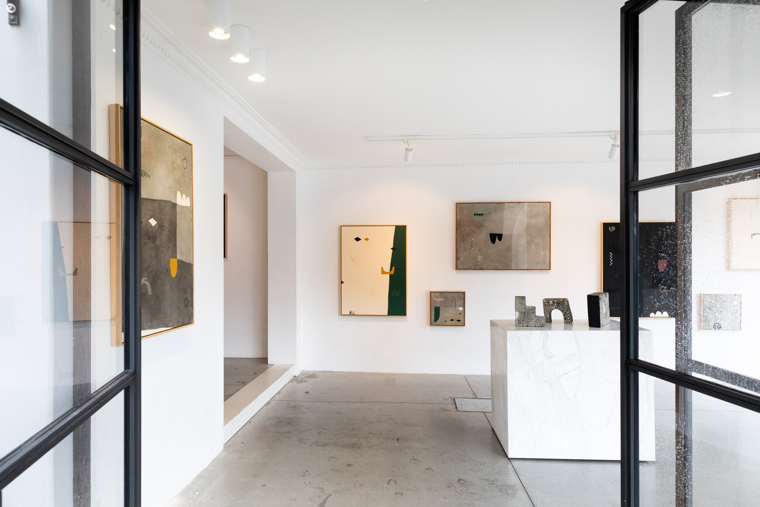 Contemporary art gallery interior with abstract paintings on the walls and sculptures on white pedestals. Bright and minimalistic design.