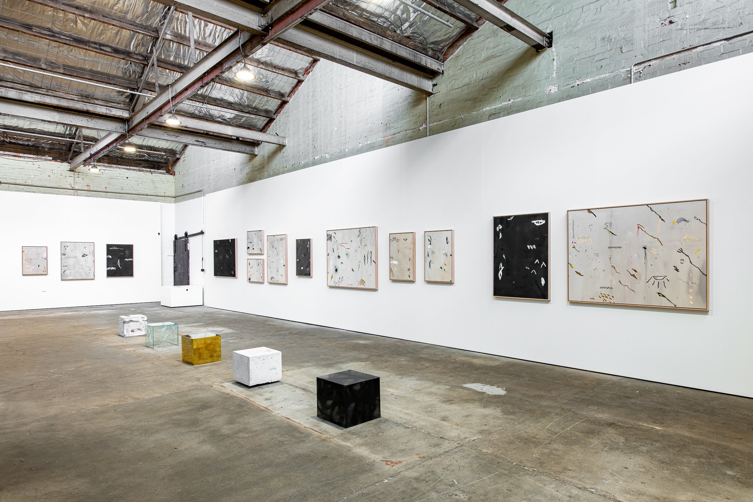 Contemporary art gallery with abstract paintings on white walls and geometric seating on concrete floor.